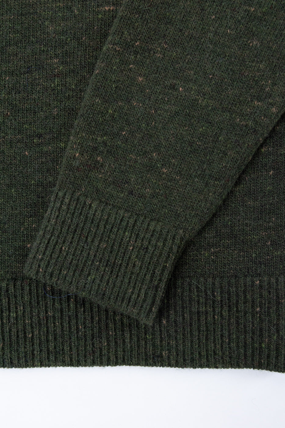 Close-up of the ribbed cuff and sleeve texture of a dark green knit sweater.