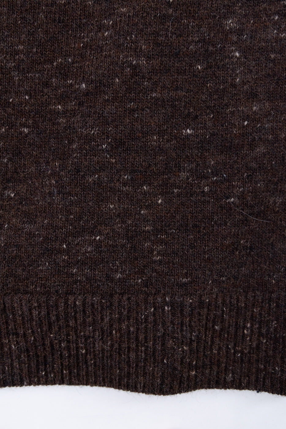 Close-up of the bottom front hem of a dark brown knit sweater with a ribbed edge.