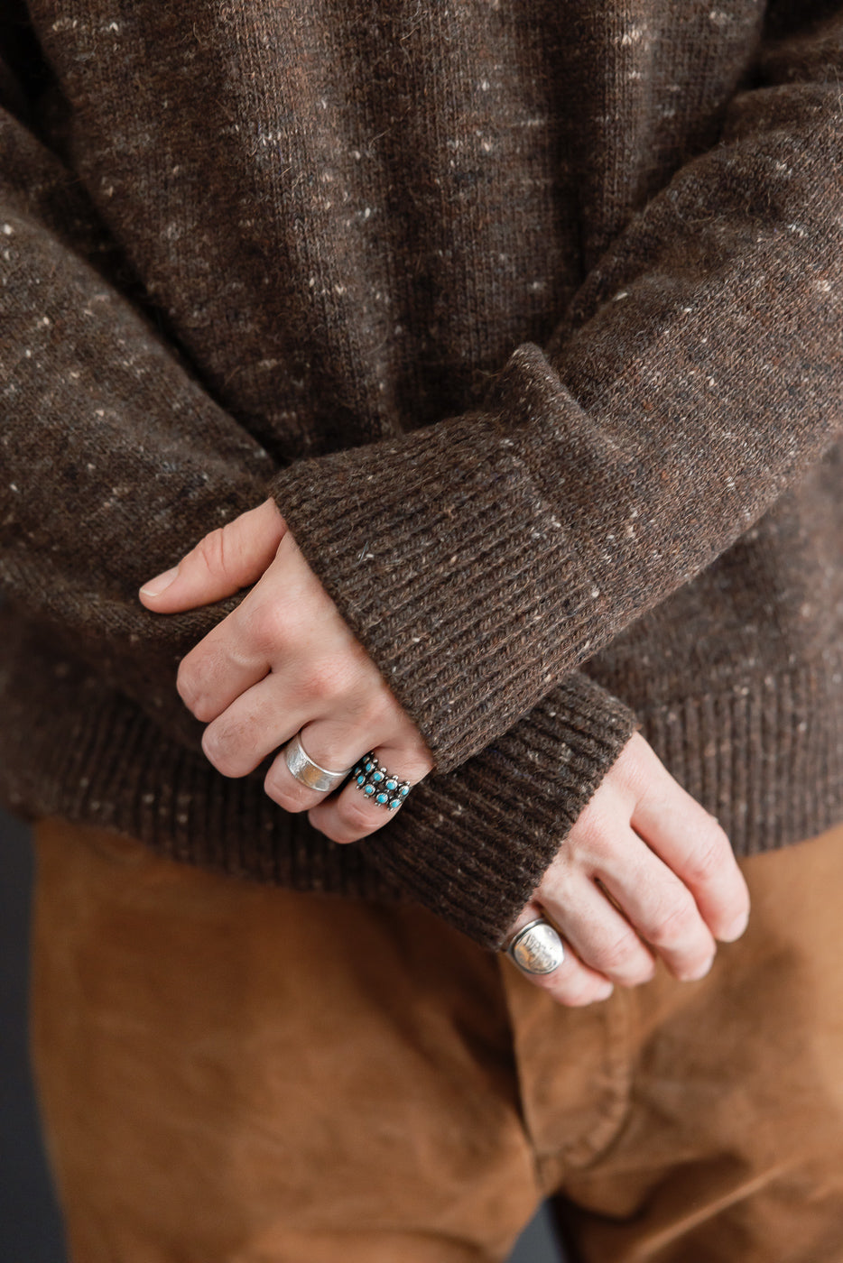 Close-up of the ribbed cuff and textured knit fabric of a brown speckled sweater.