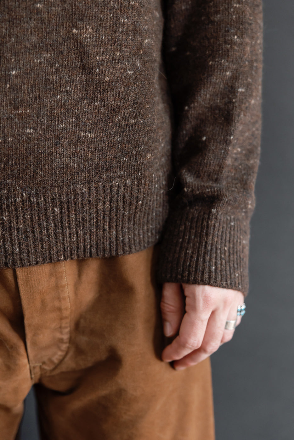 Close-up of the front hem and ribbed cuff of a brown speckled knit sweater on a 5'9