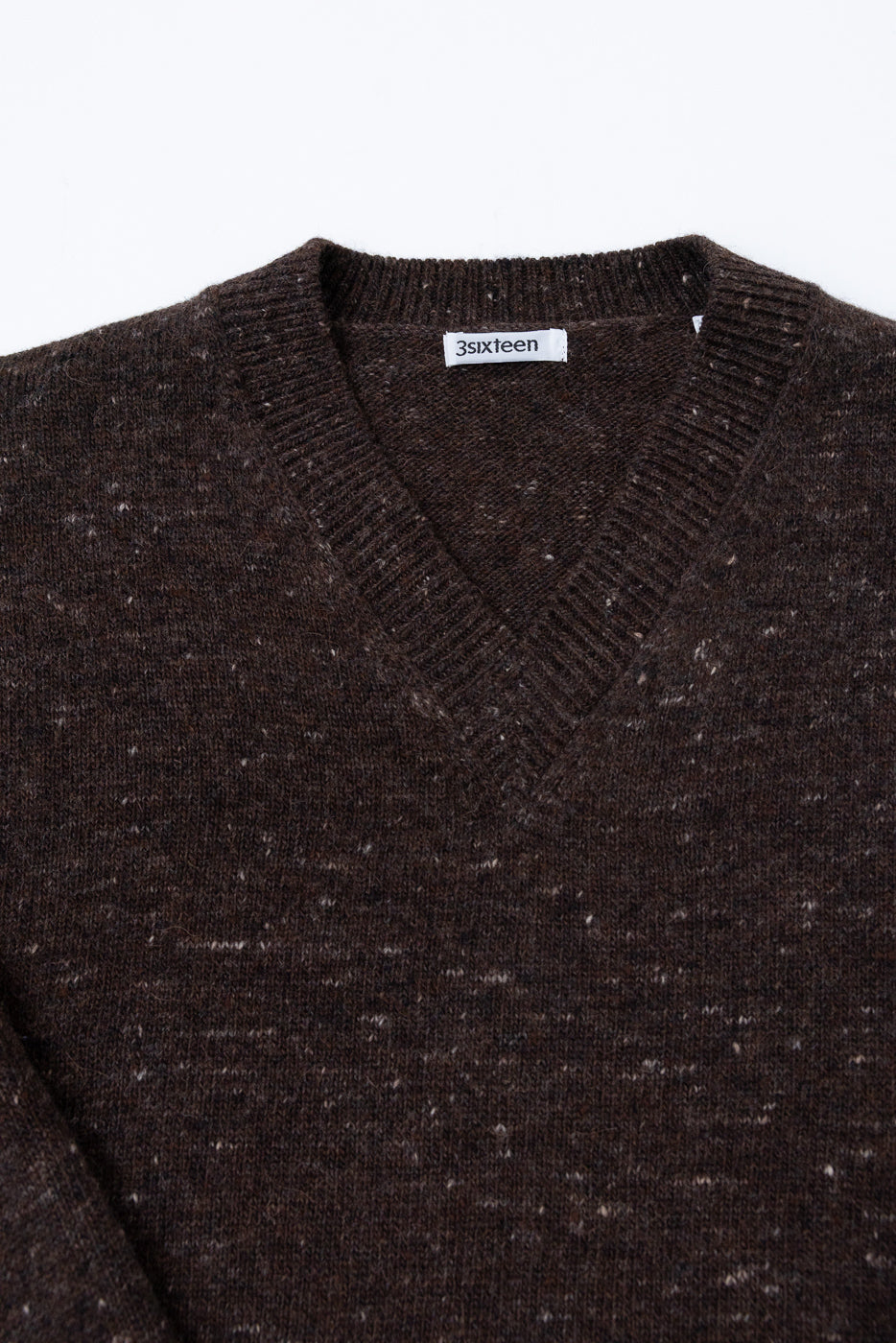Close-up of the front v-neck collar and 3sixteen brand tag of a brown textured knit sweater.