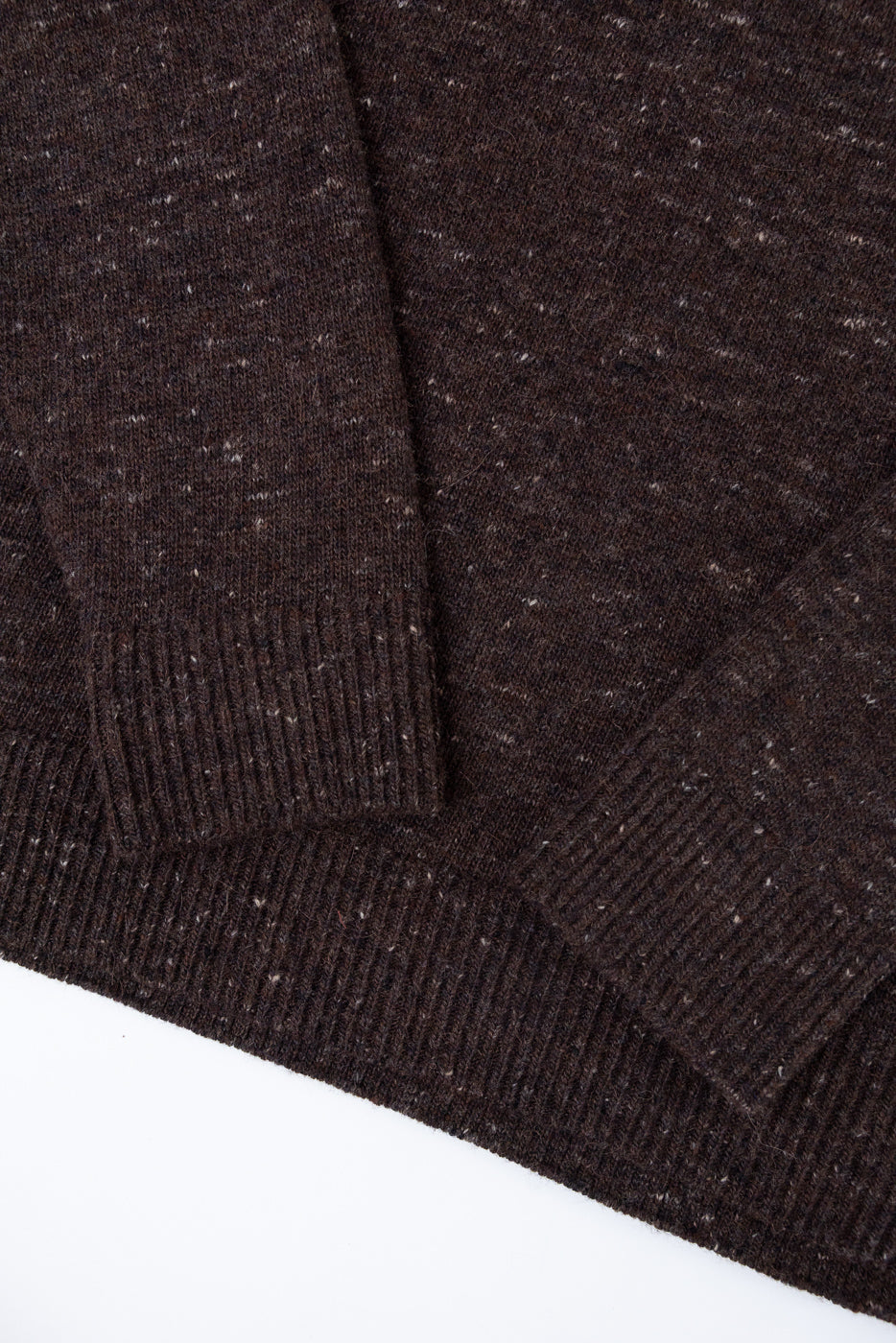 Close-up of the front and sleeve showing the ribbed cuff and speckled texture of a brown sweater.