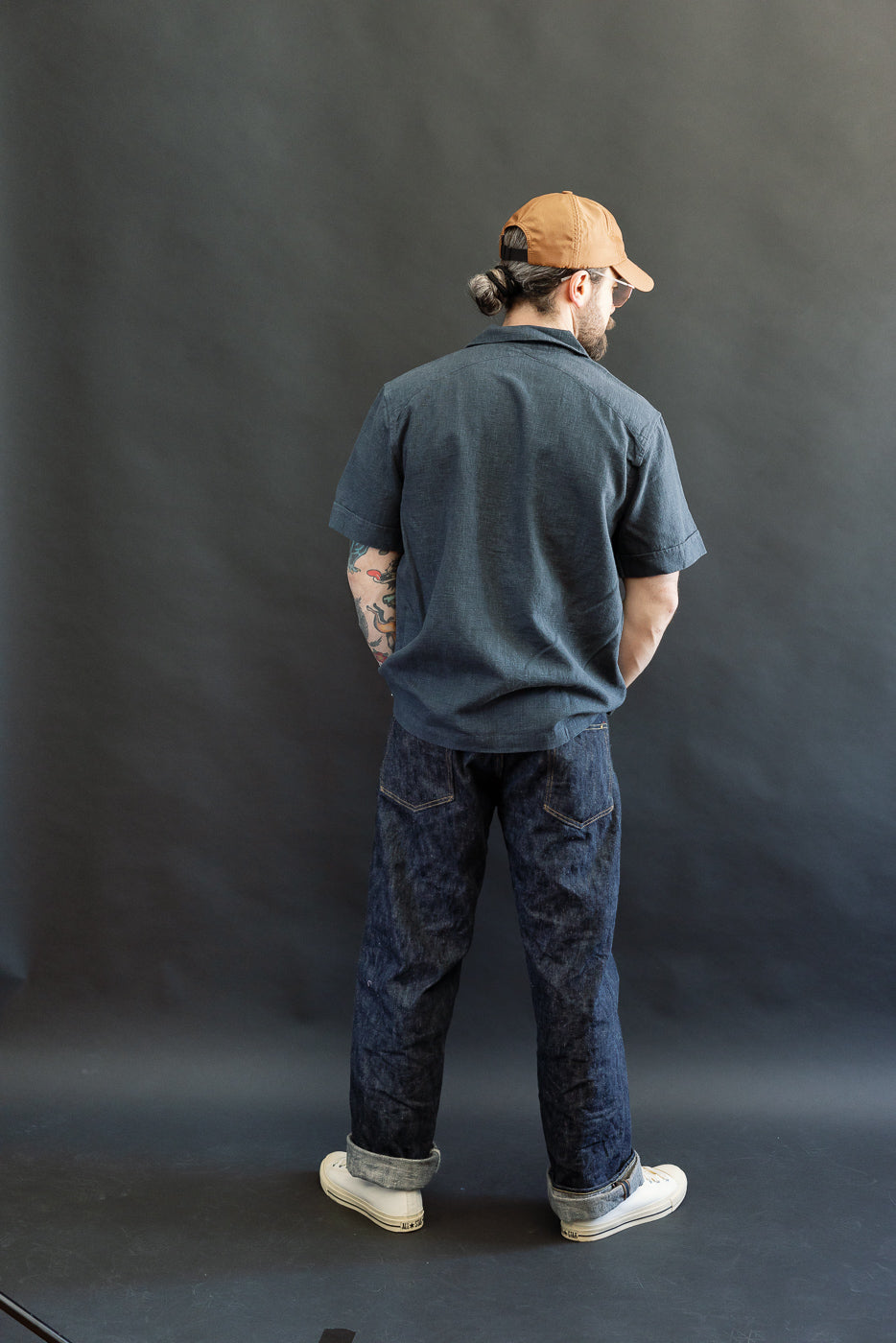 Man wearing Vacation Shirt - Blue Linen, showcasing its 1950s-inspired open collar, coconut buttons, and relaxed fit. Paired with denim jeans and sneakers, reflecting Dant's heritage-inspired menswear style.