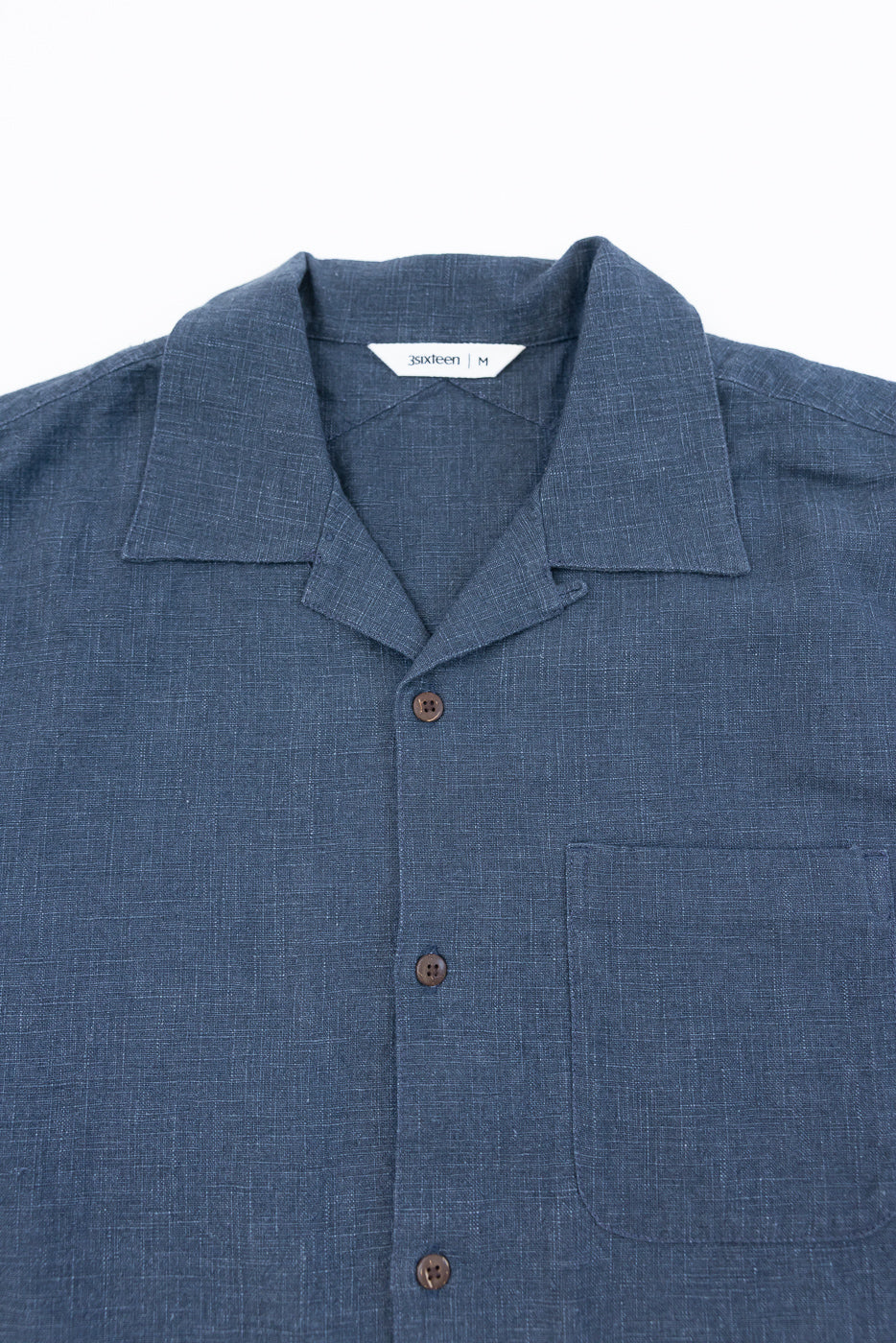 Vacation Shirt - Blue Linen: A men's medium short-sleeve, navy-blue button-up with a camp collar, three coconut buttons, and a chest pocket, crafted from soft, enzyme-washed 100% linen.