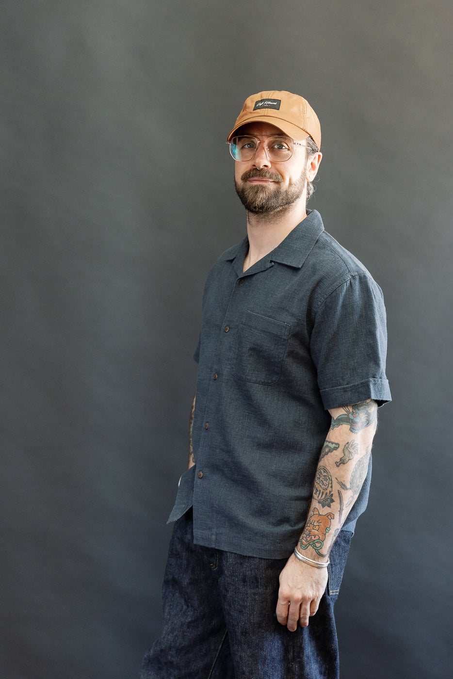 Man in a short-sleeved, dark blue Vacation Shirt - Blue Linen, showcasing its relaxed fit, open collar, and coconut buttons, styled with dark denim pants, embodying Dant's premium menswear aesthetic.