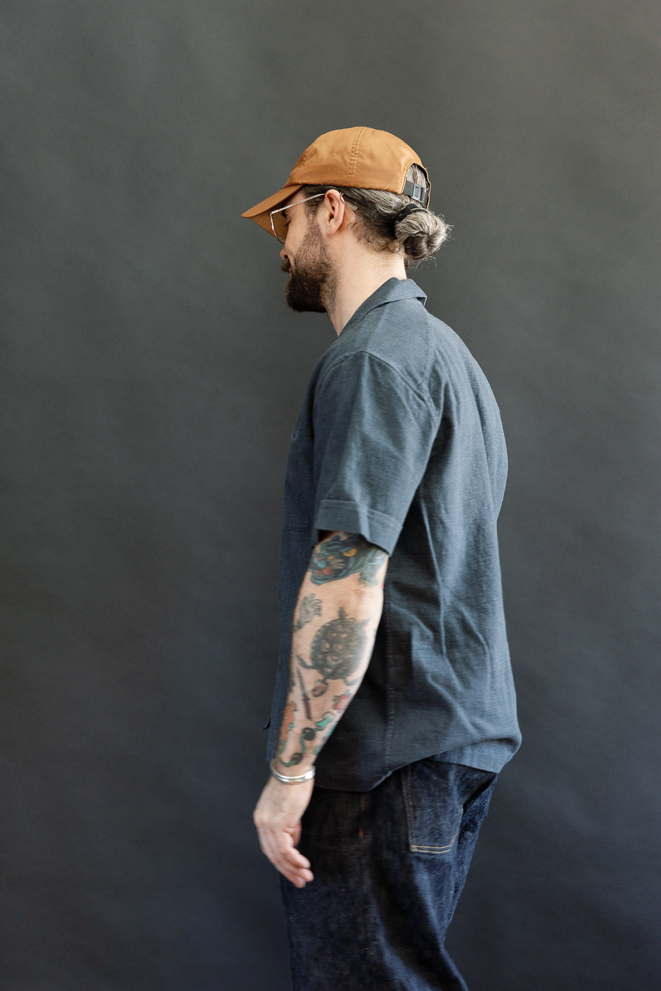 A man models the 3sixteen Vacation Shirt in blue linen, showcasing its relaxed fit, open collar, and single chest pocket. The shirt epitomizes vintage-inspired, modern menswear.