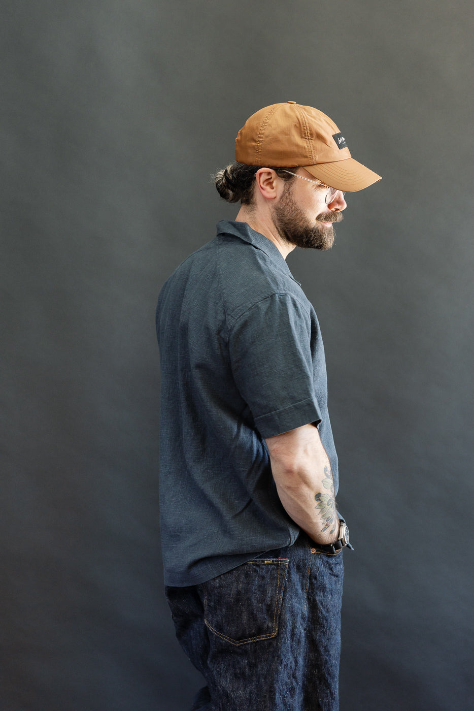 A model showcases the Vacation Shirt - Blue Linen, styled untucked over dark denim jeans, emphasizing its relaxed fit and open collar.