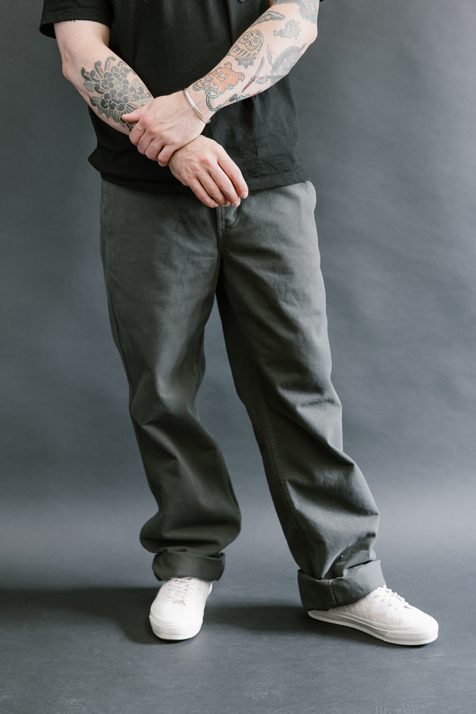 Person wearing dark gray pants and white shoes on a gray background