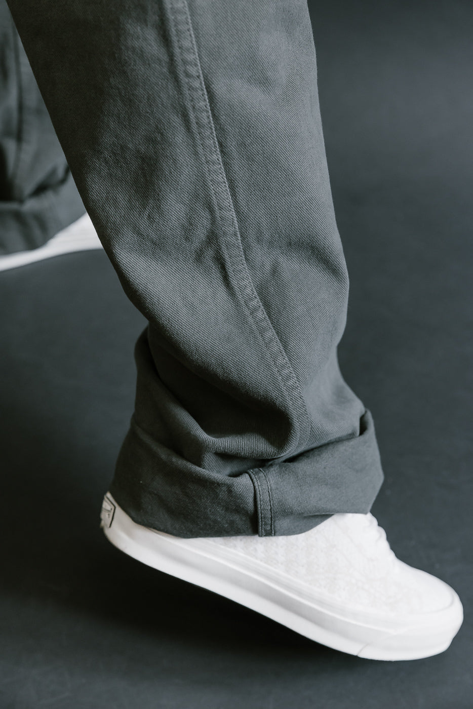 Person wearing dark gray pants and white sneakers on a black background
