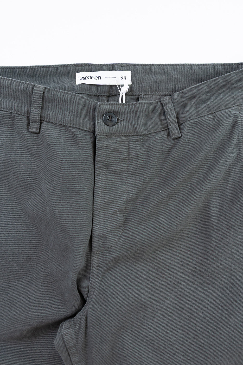 Close-up of dark gray pants with a brand label on a white background