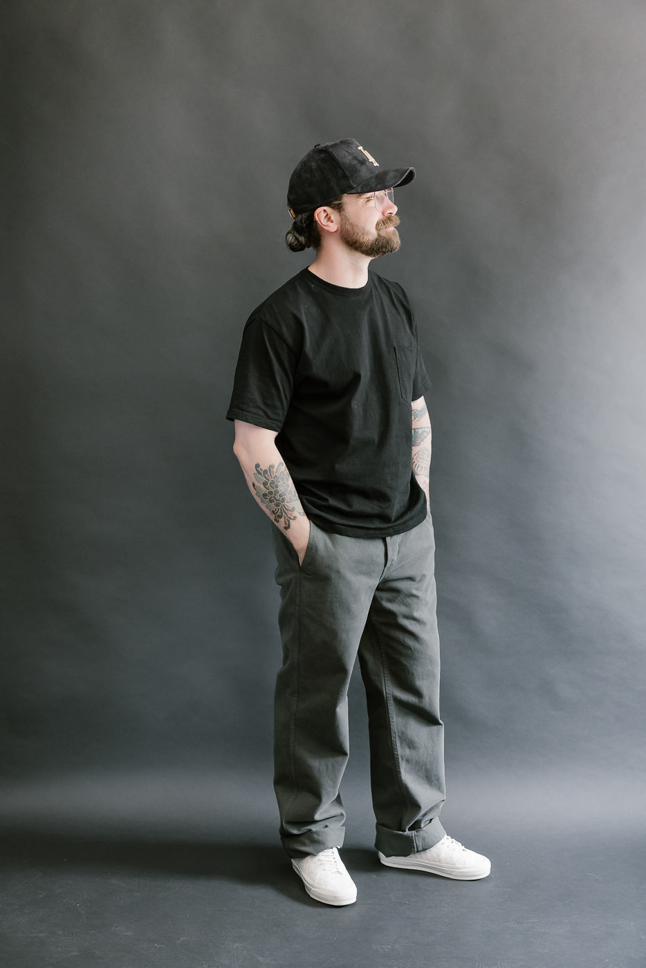 Man wearing a black t-shirt, gray pants, and a black cap against a gray background