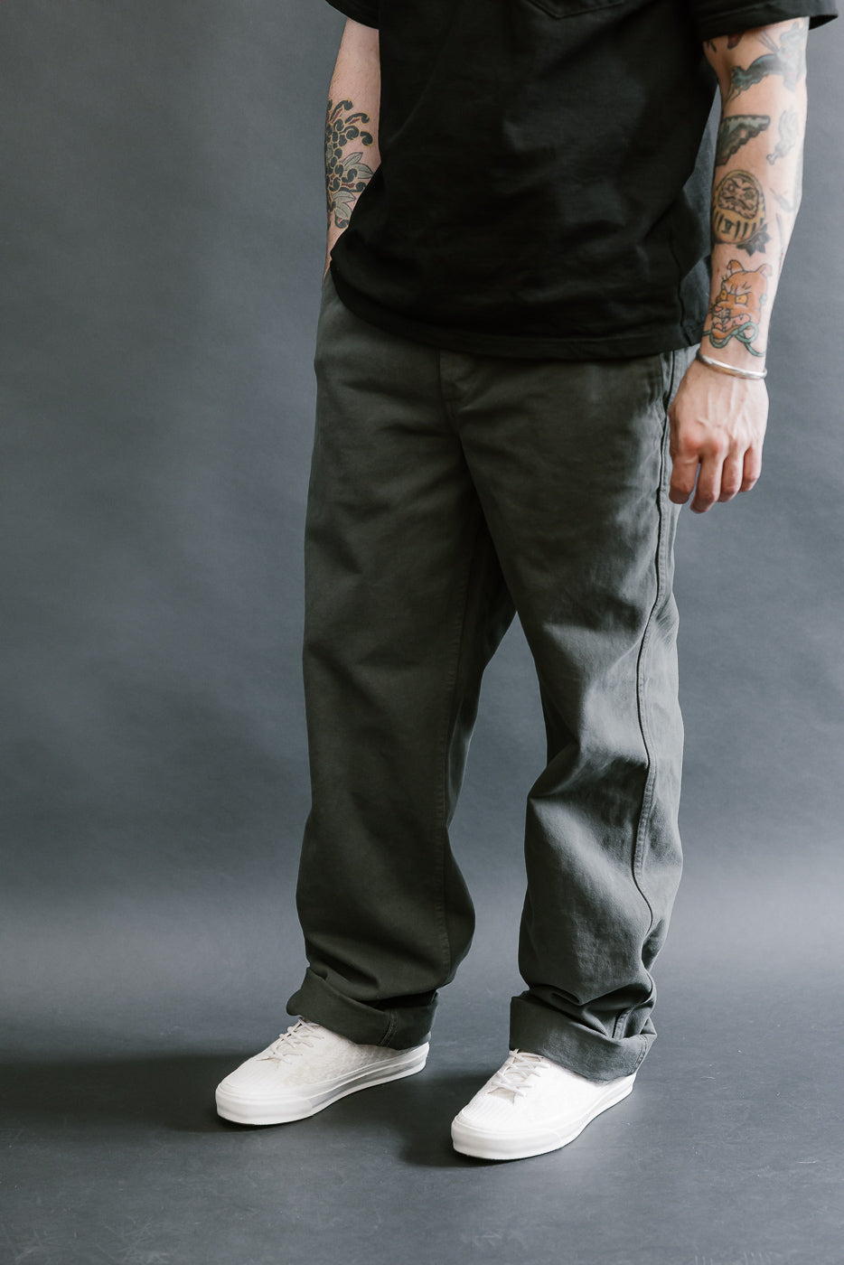 Person wearing black shirt, gray pants, and white shoes against a gray background