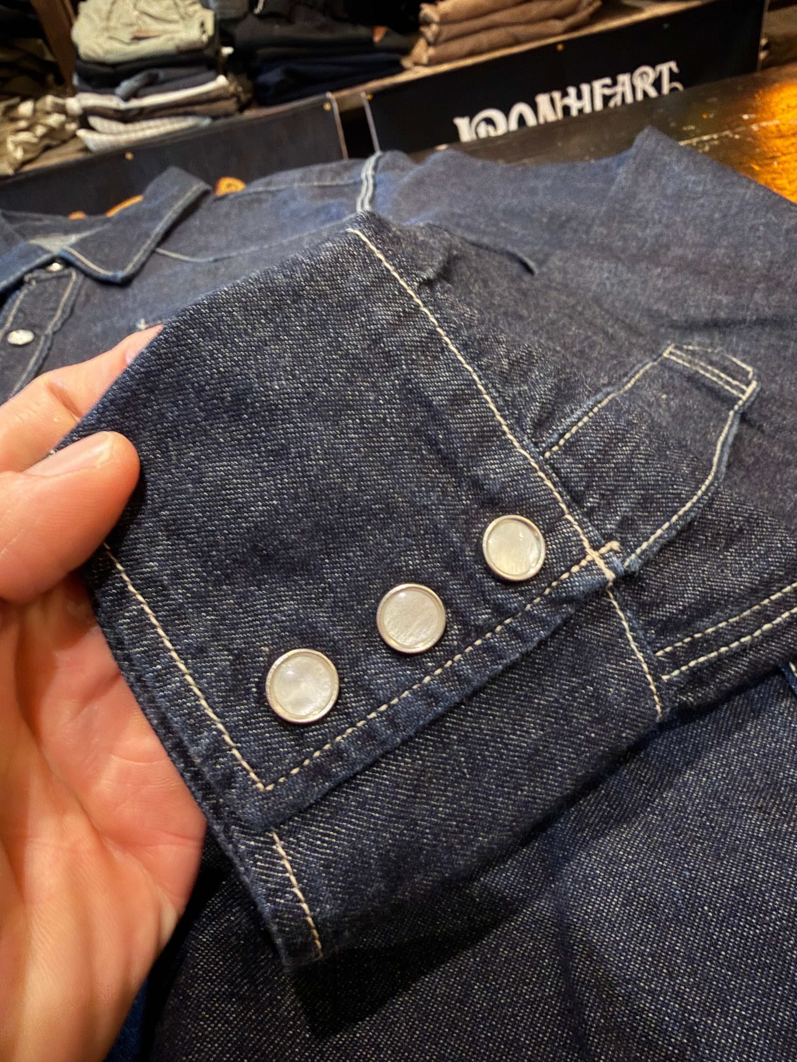 Close-up of denim shirt sleeve cuff, showcasing three metal buttons and visible stitching.