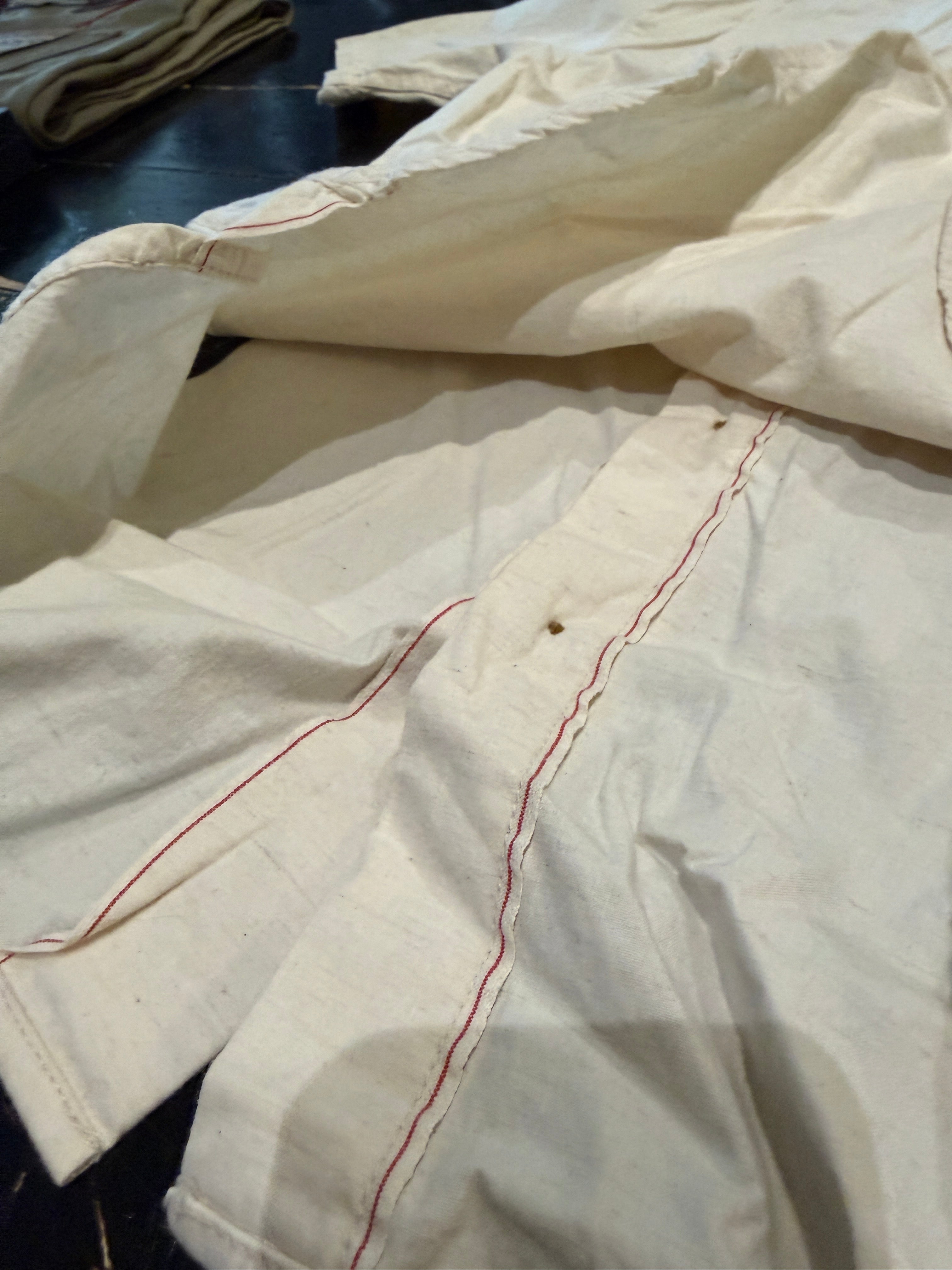 Close-up of cream shirt laid flat, showing inside seam with red contrast stitching and hem detail.