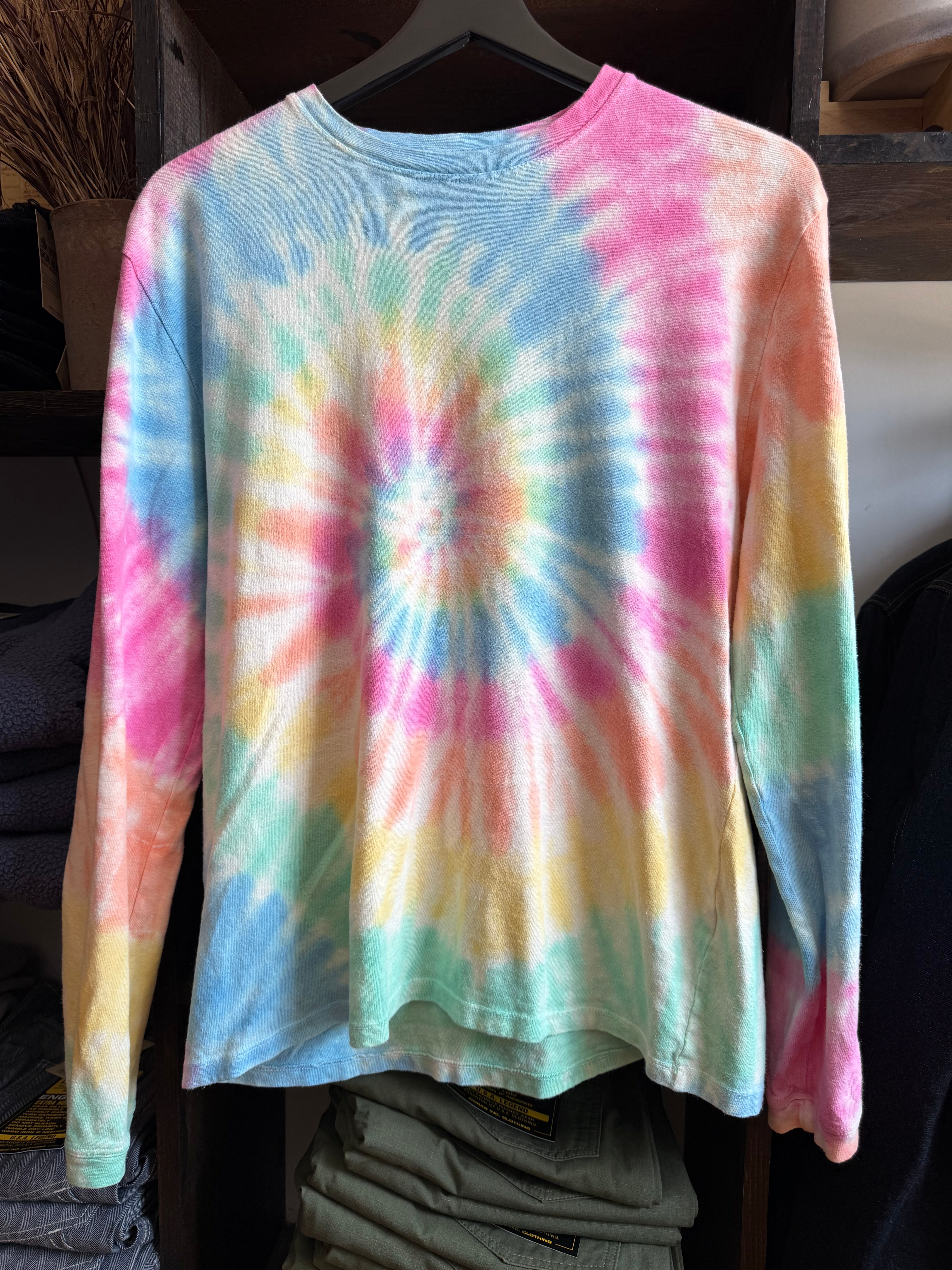 Front view of a pastel tie-dye long-sleeve shirt with vibrant swirls, displayed on a hanger.