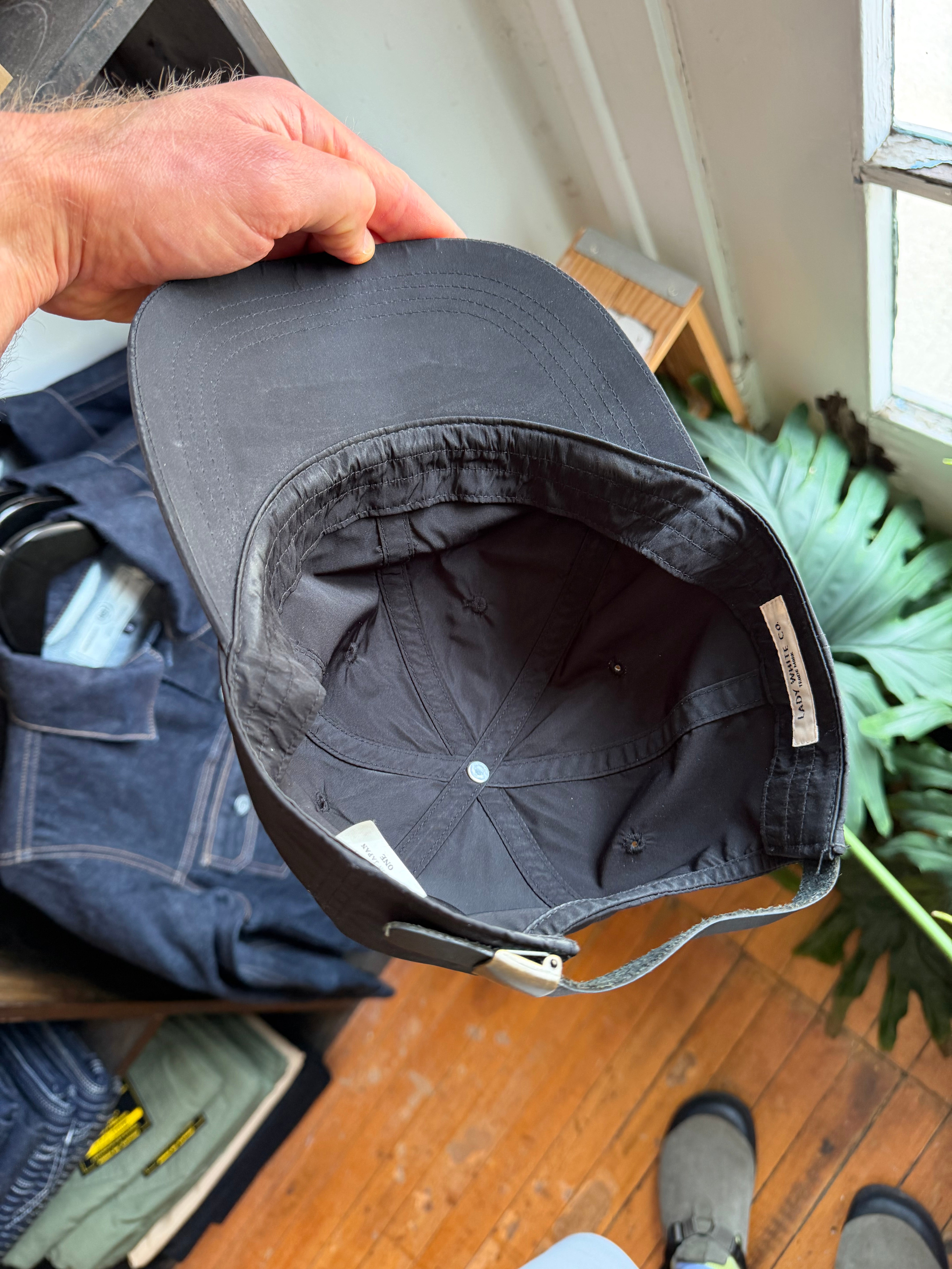 Close-up of black cap's interior, showing tag and adjustable strap, held by hand