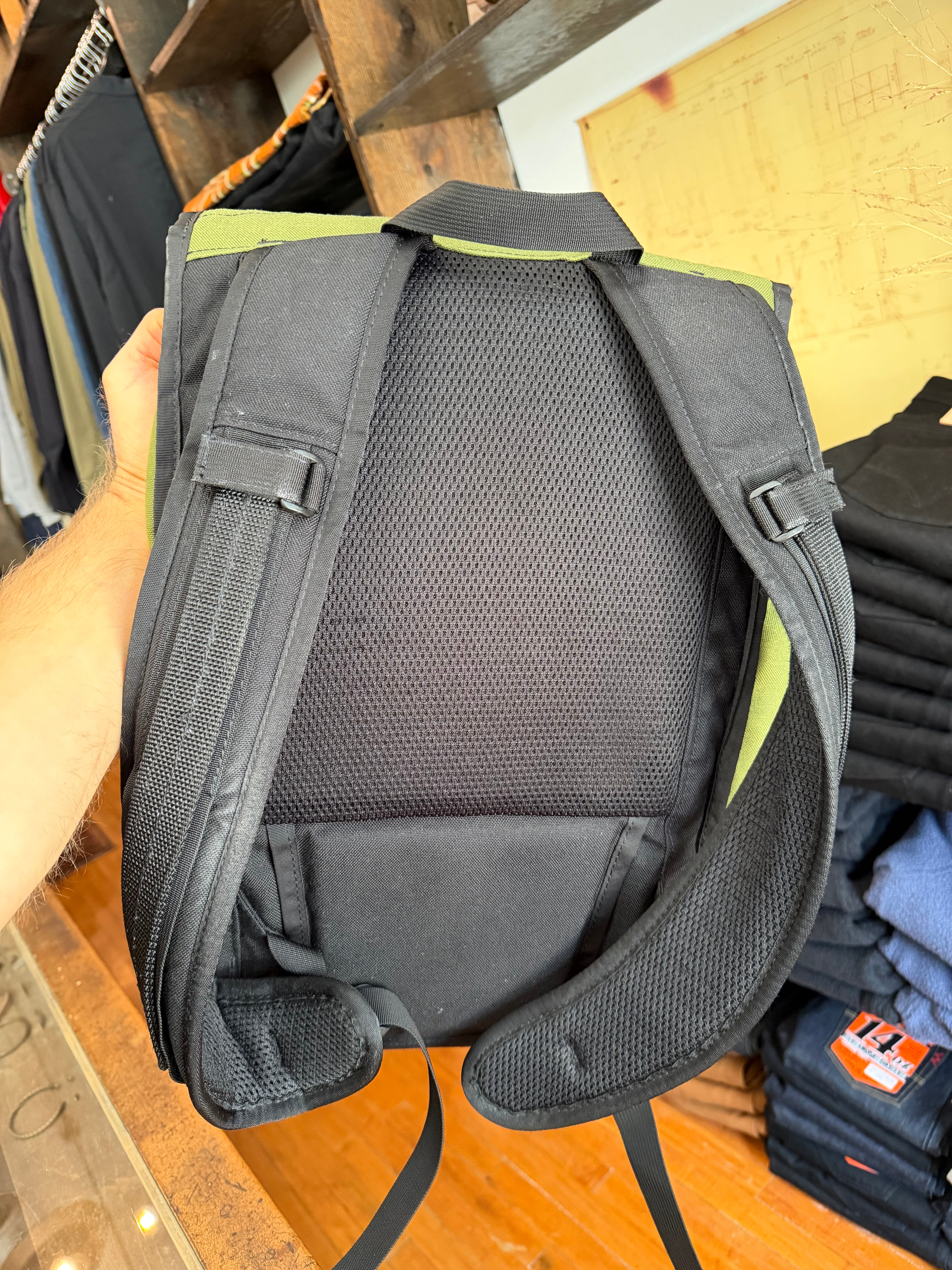Close-up of black backpack back panel with mesh padding, adjustable straps, and lime green accents, held in hand.