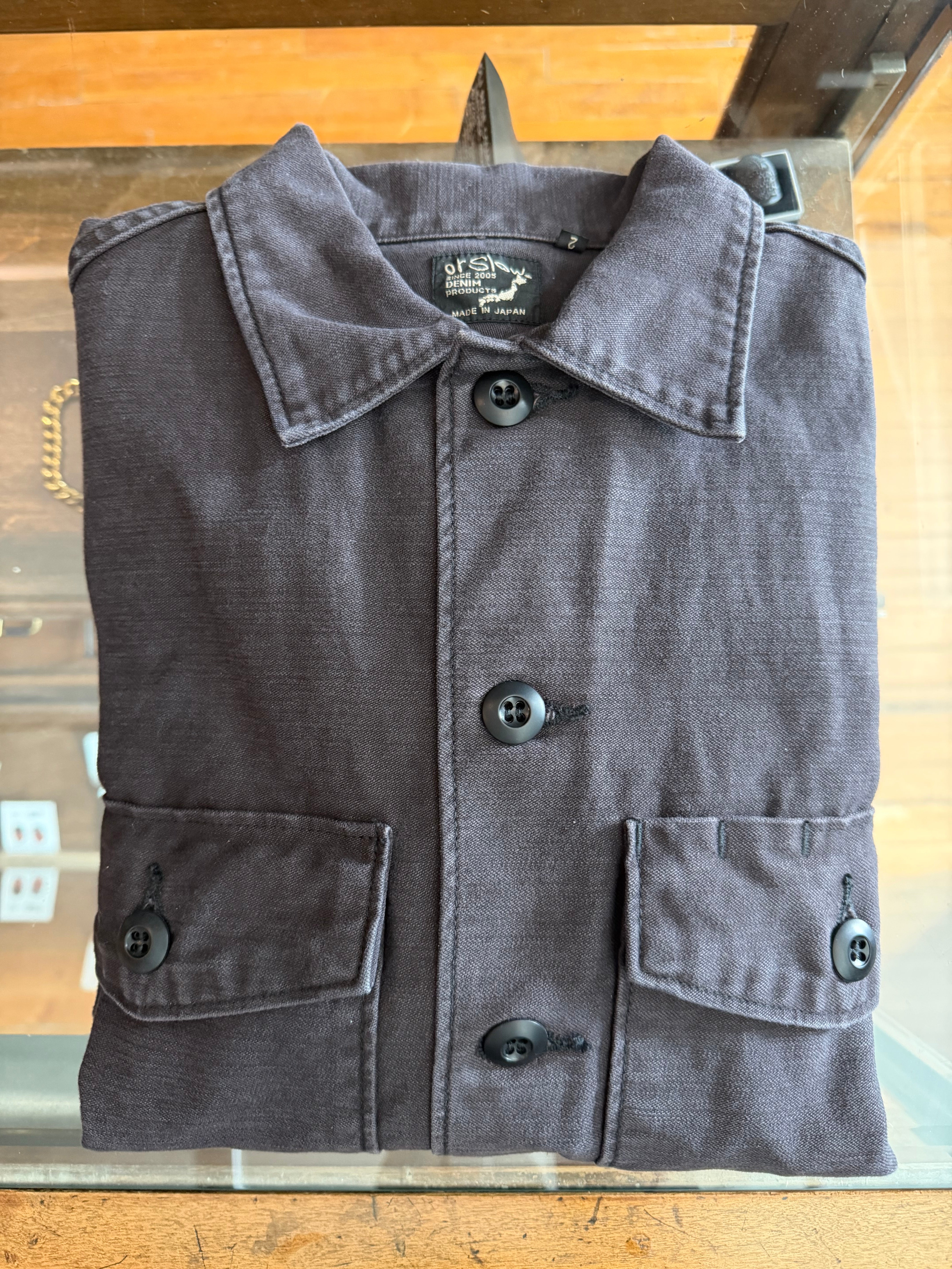 Folded black Japanese-made denim jacket, front view, collar, buttons, and flap pockets visible