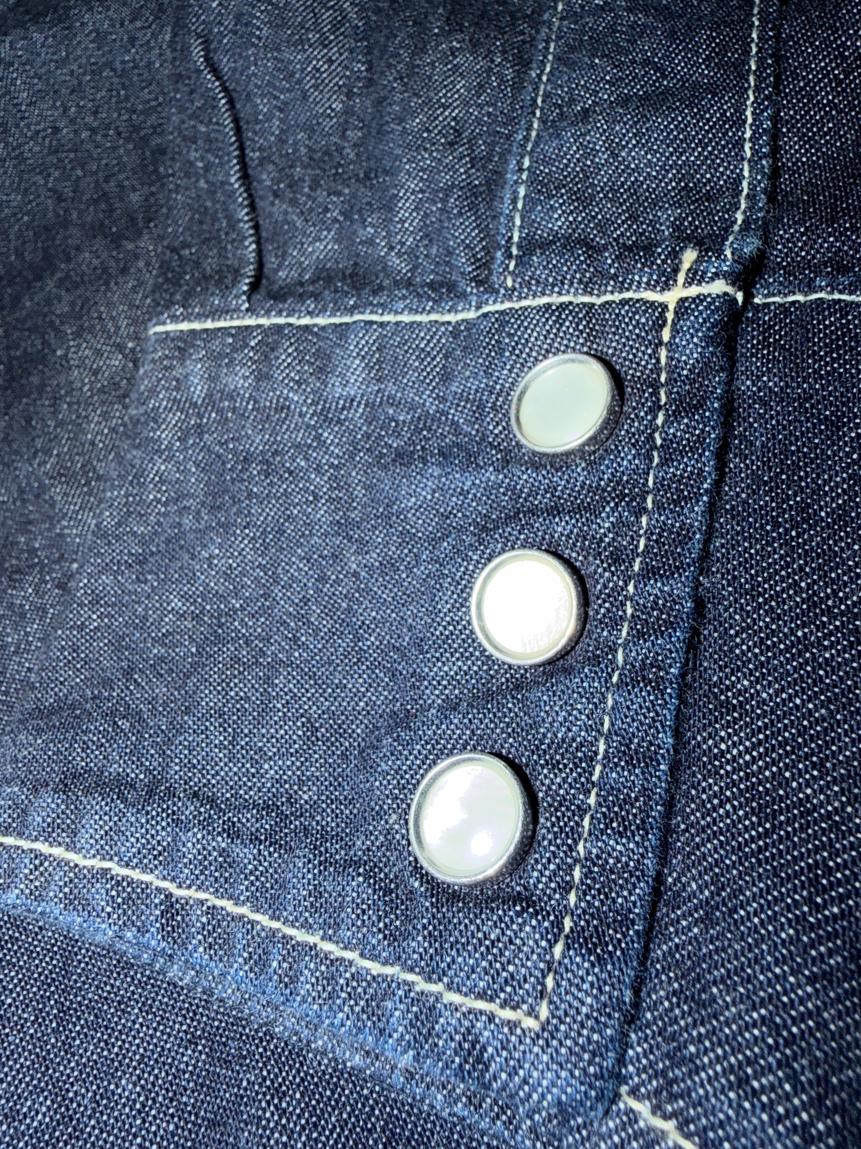 Denim jacket front close-up, focusing on pocket detail, metal buttons, and contrast stitching.