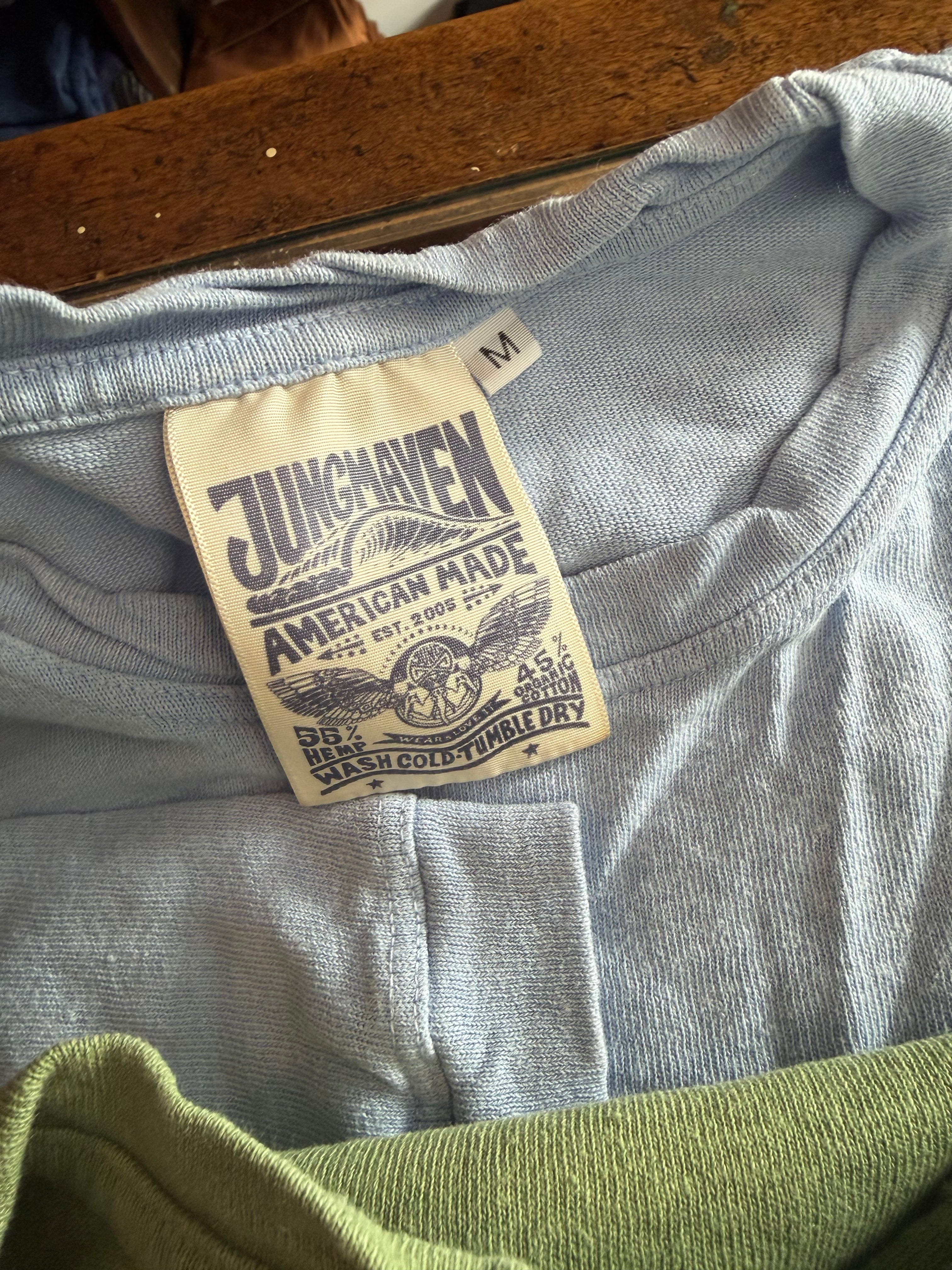 Close-up of blue Jungmaven t-shirt neckline showing size M and fabric tag details, front view