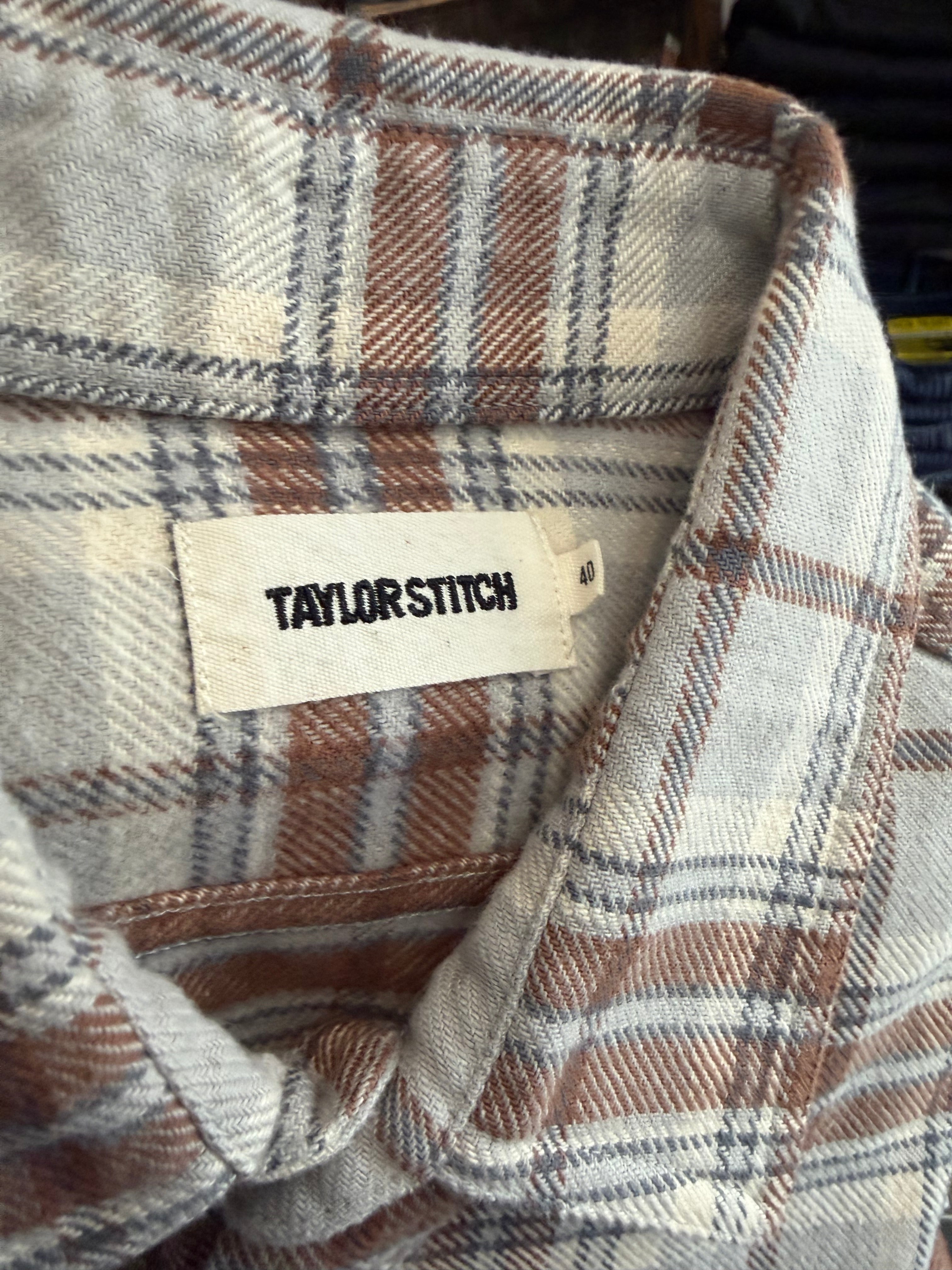 Close-up of Taylor Stitch men's plaid shirt collar, showing fabric texture and woven tag, front view.