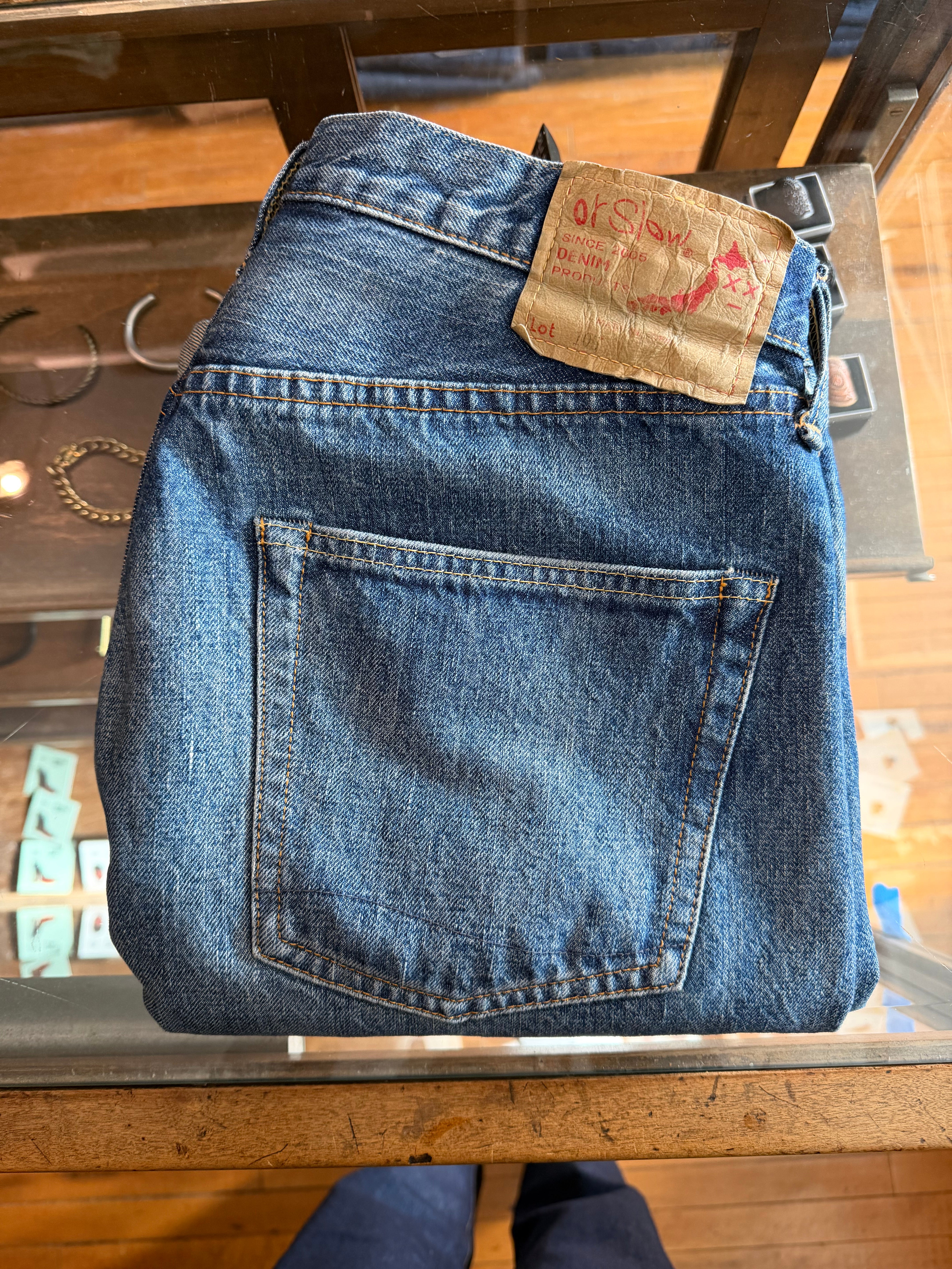 Close-up of folded selvedge denim jeans back side, visible rear pocket and leather brand patch, displayed on a shop counter at Dant Indianapolis.