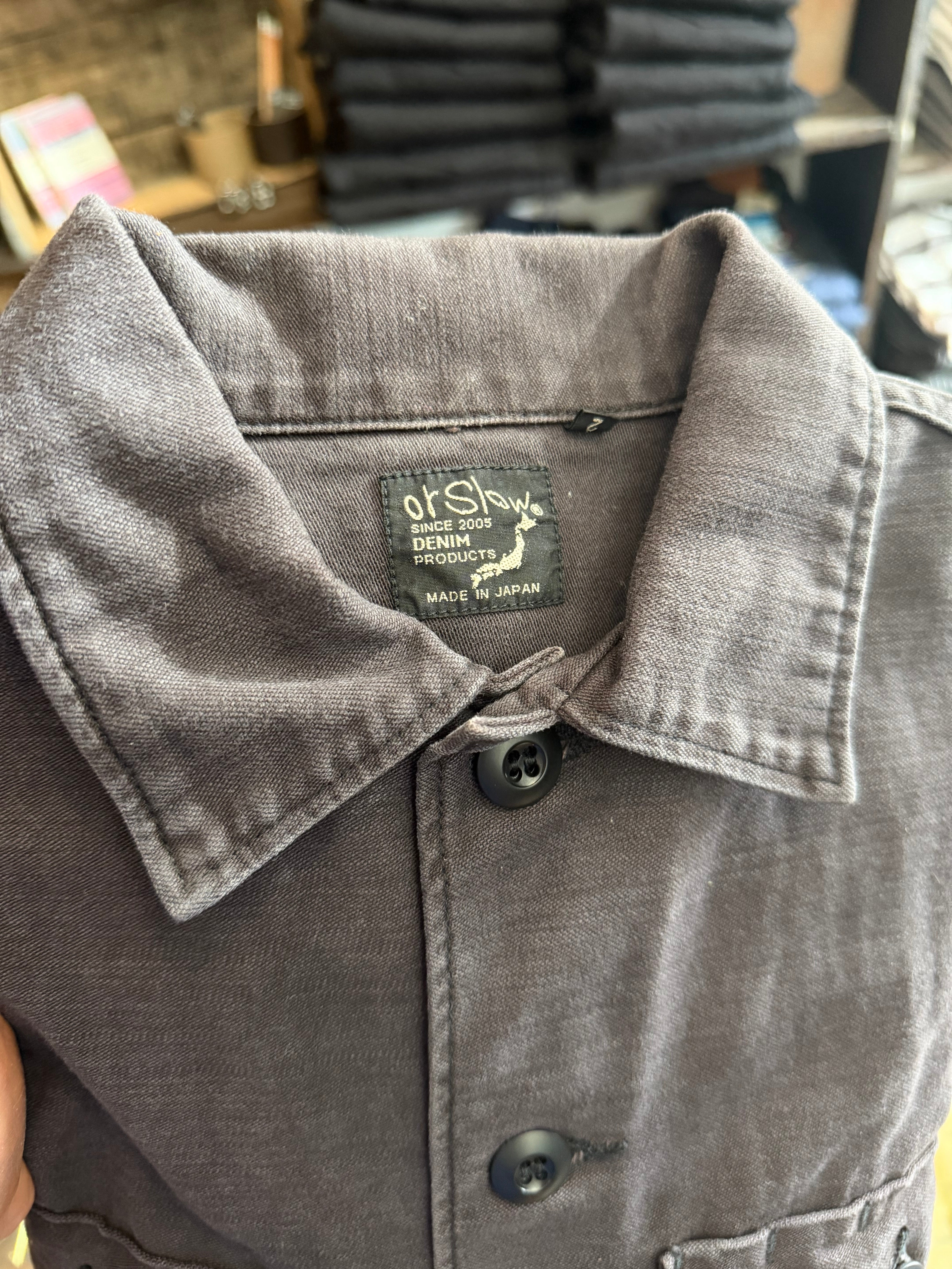 Close-up of orSlow denim jacket front, showing collar, buttons, and chest tag detail at Dant shop.