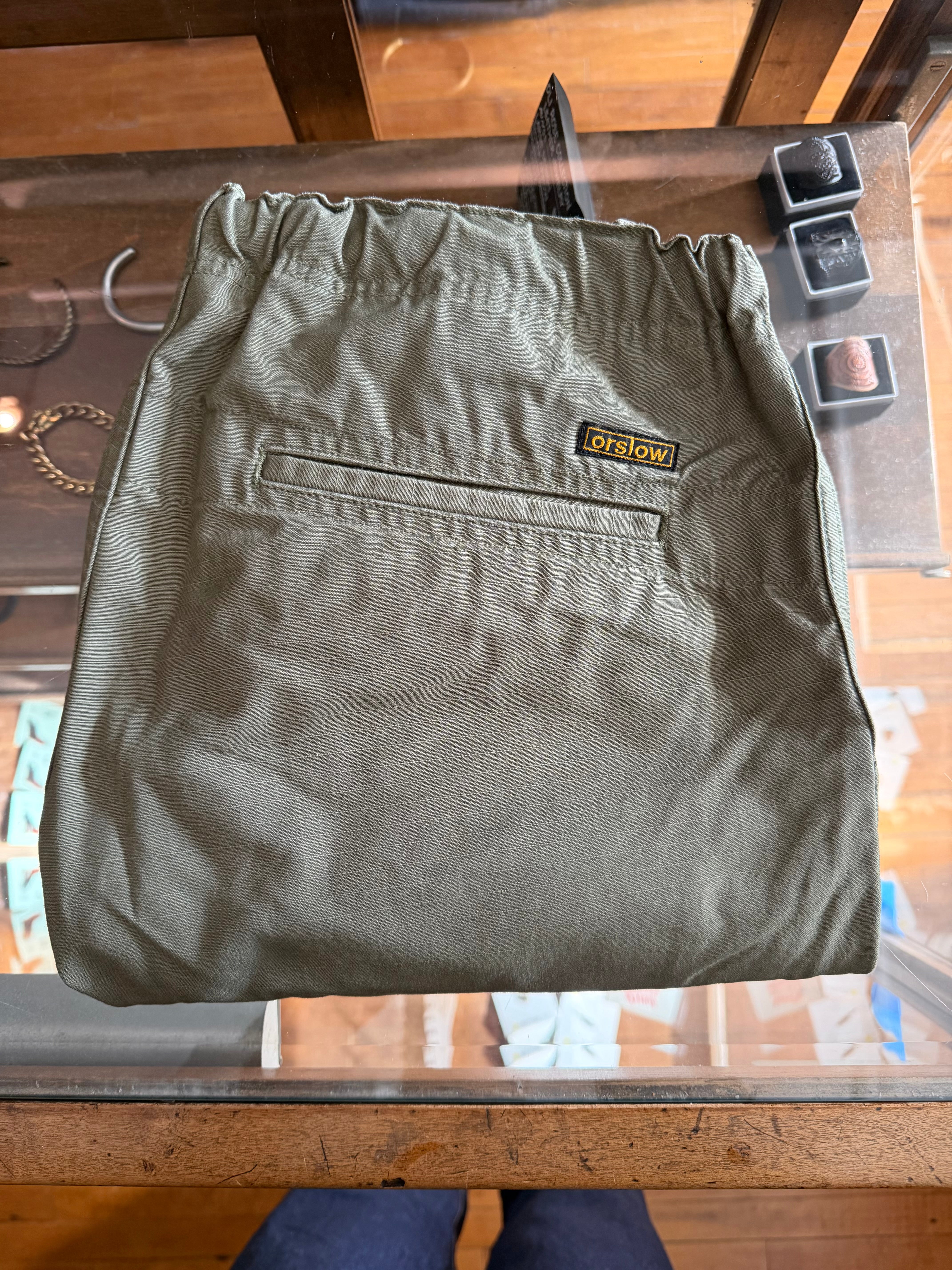 Flat lay of orSlow olive green pants, elastic waistband, back view with rear pocket and logo tag.