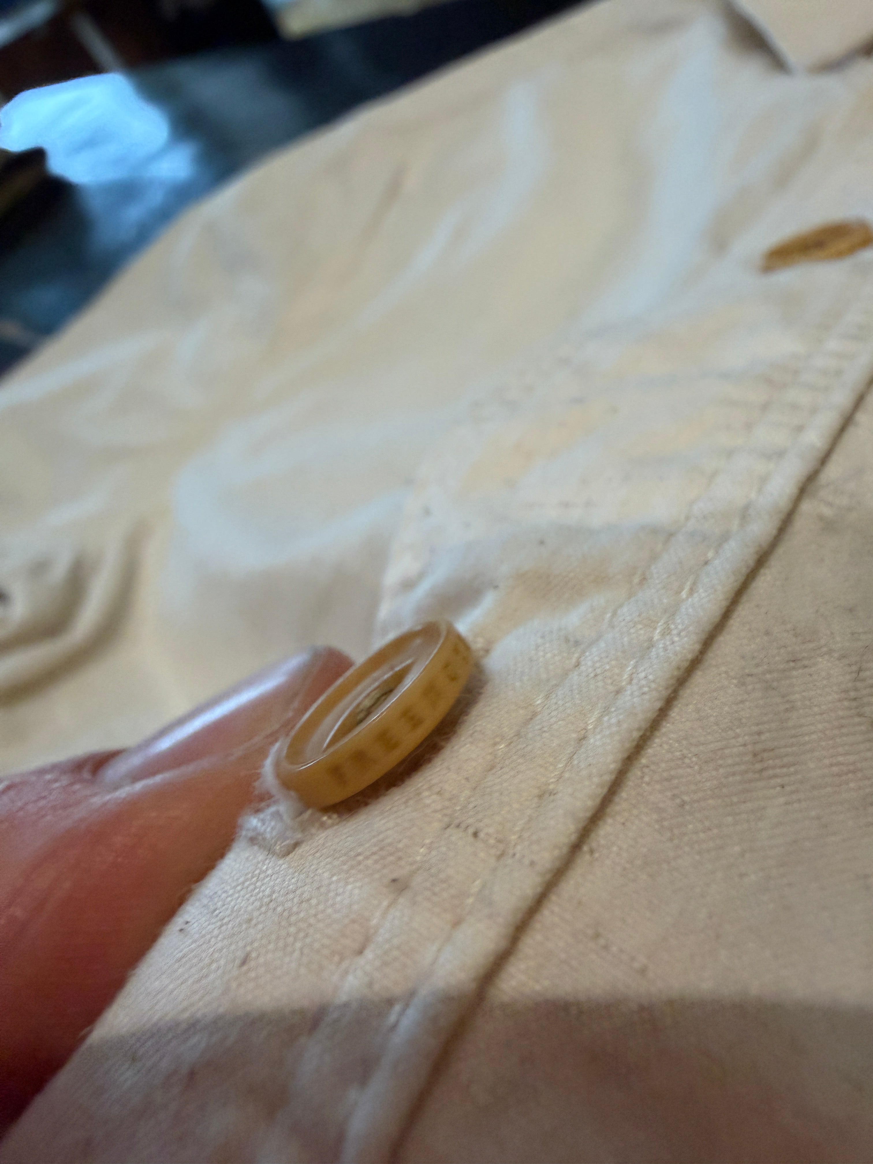 Close-up of beige shirt front, highlighting tan button and textured fabric stitching.