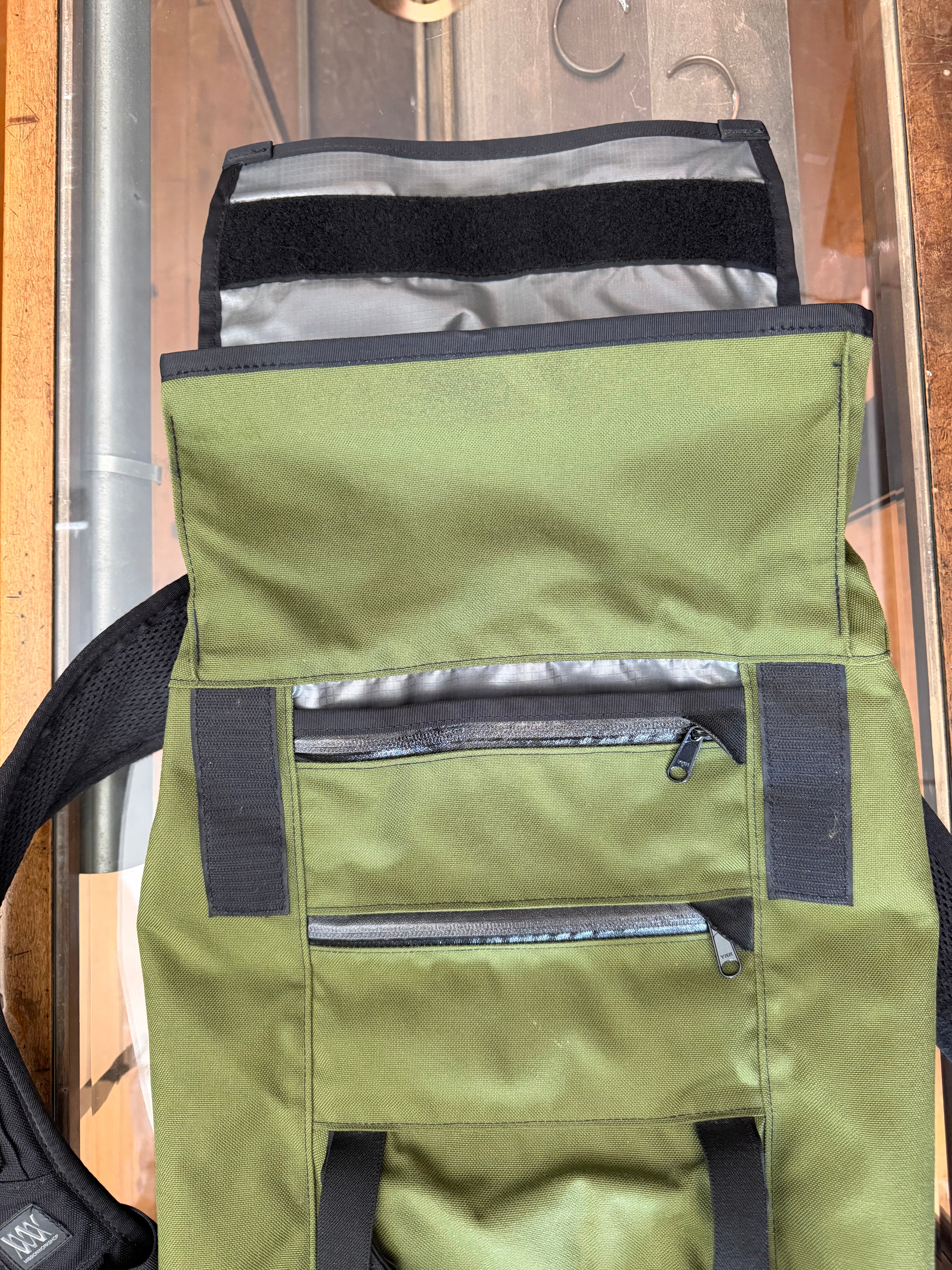Olive green backpack front view, close-up of zippered pockets and fabric texture