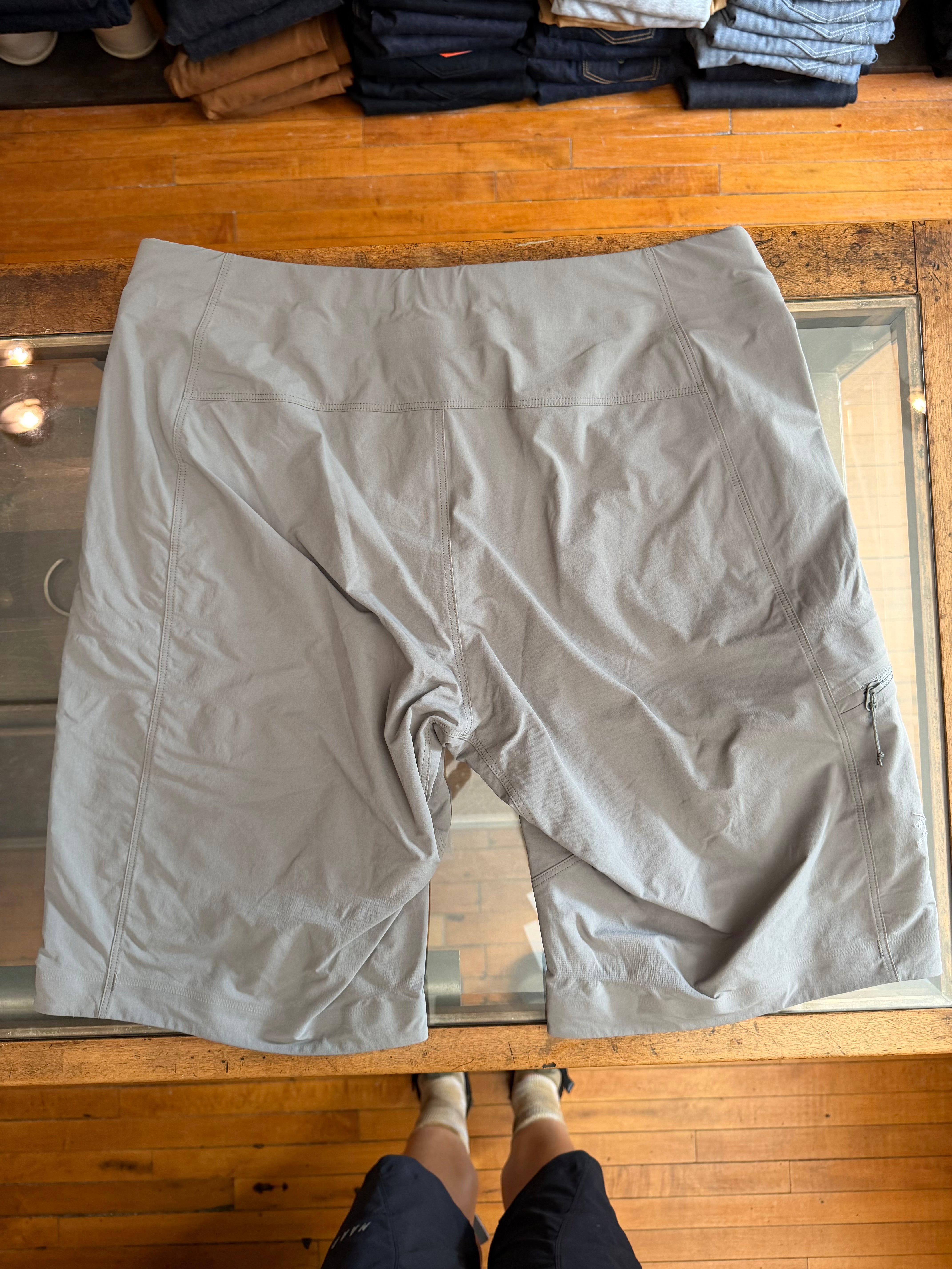 Flat lay front view of light gray men's shorts with zip pocket, laid on glass table over wood floor