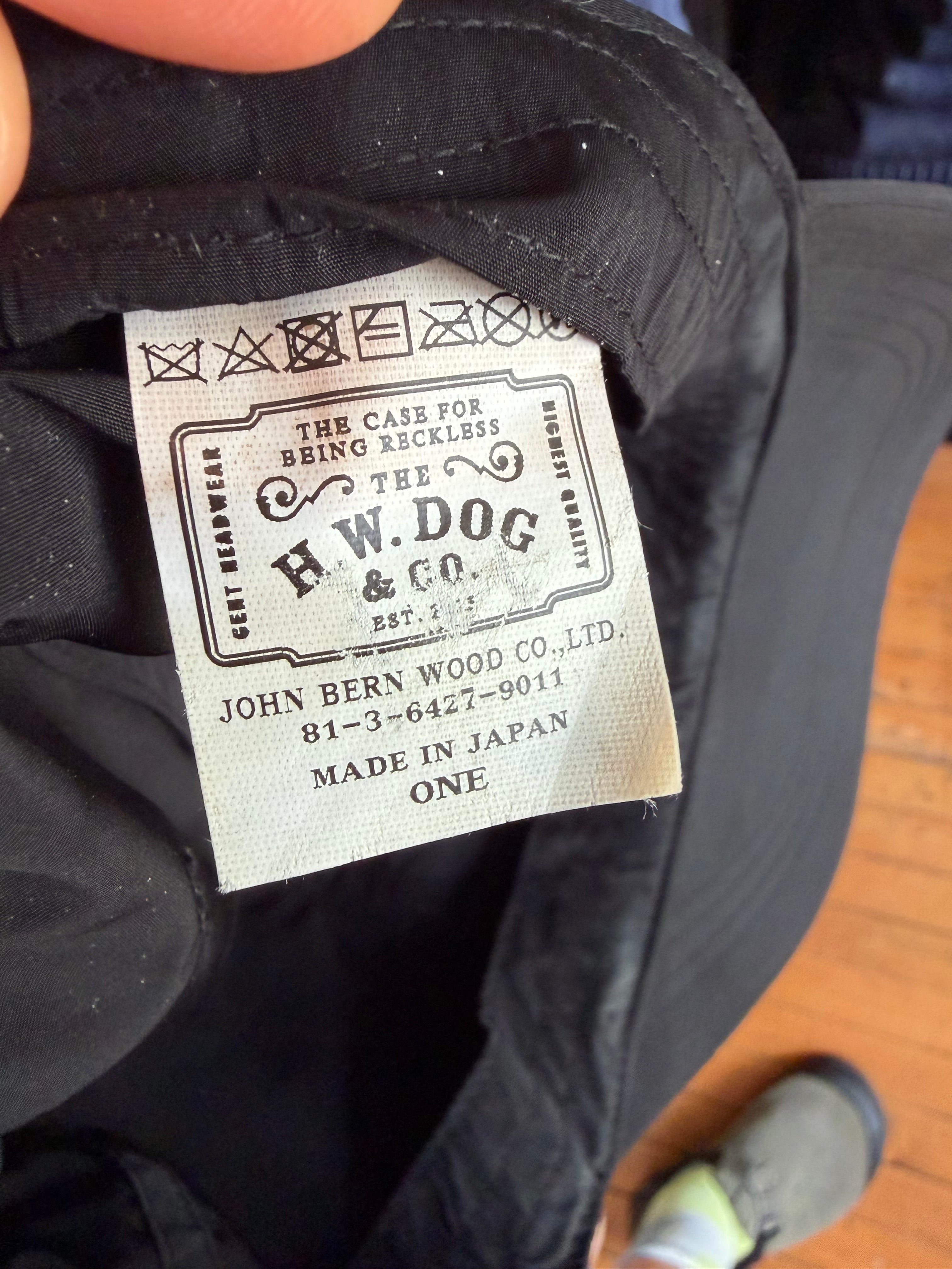Close-up of H.W. Dog & Co. hat tag, showing 'Made in Japan' label, care symbols, and brand details on black headwear.