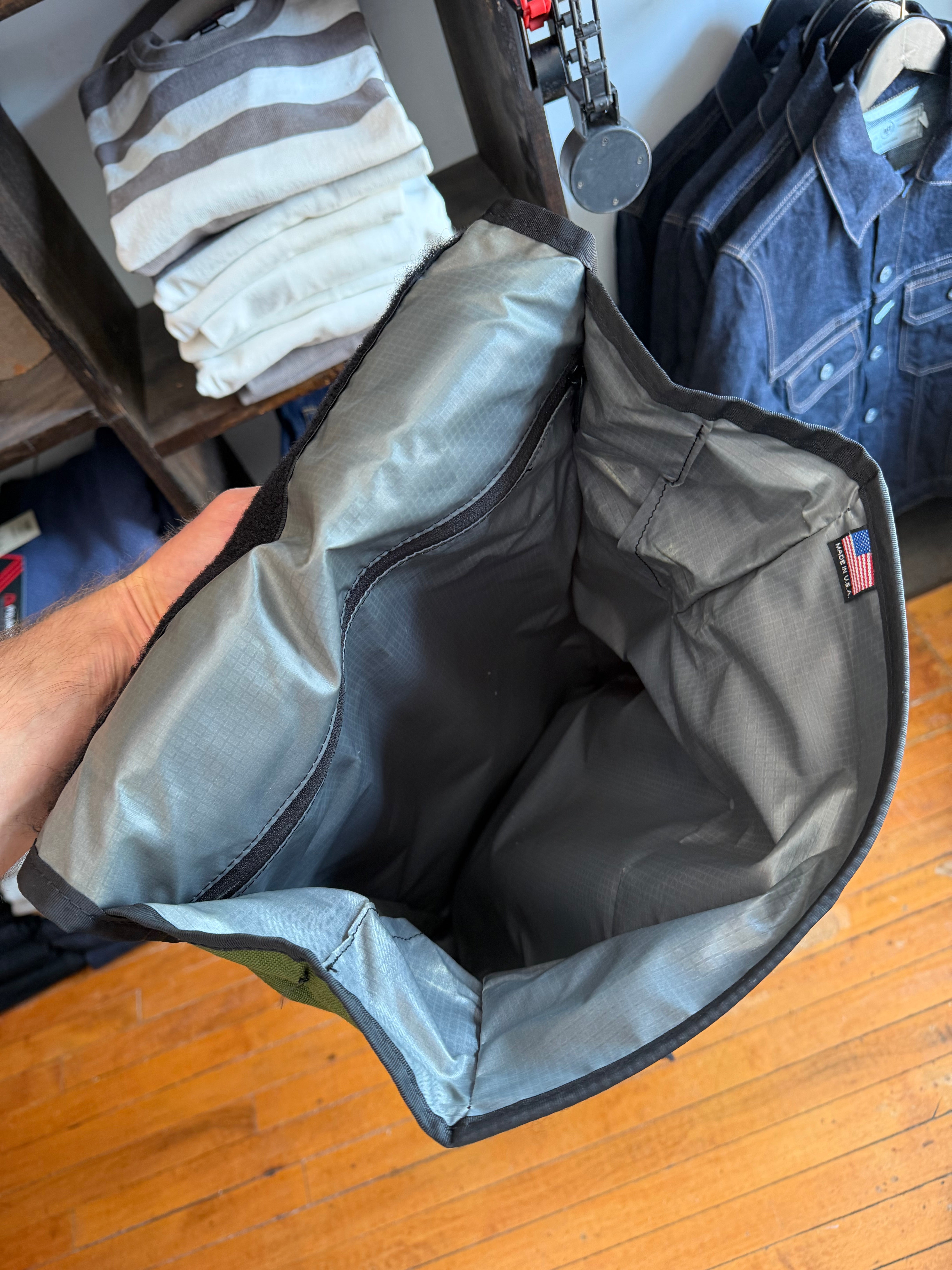 Close-up of gray bag interior, showing durable fabric, black trim, and USA flag tag, held by hand.