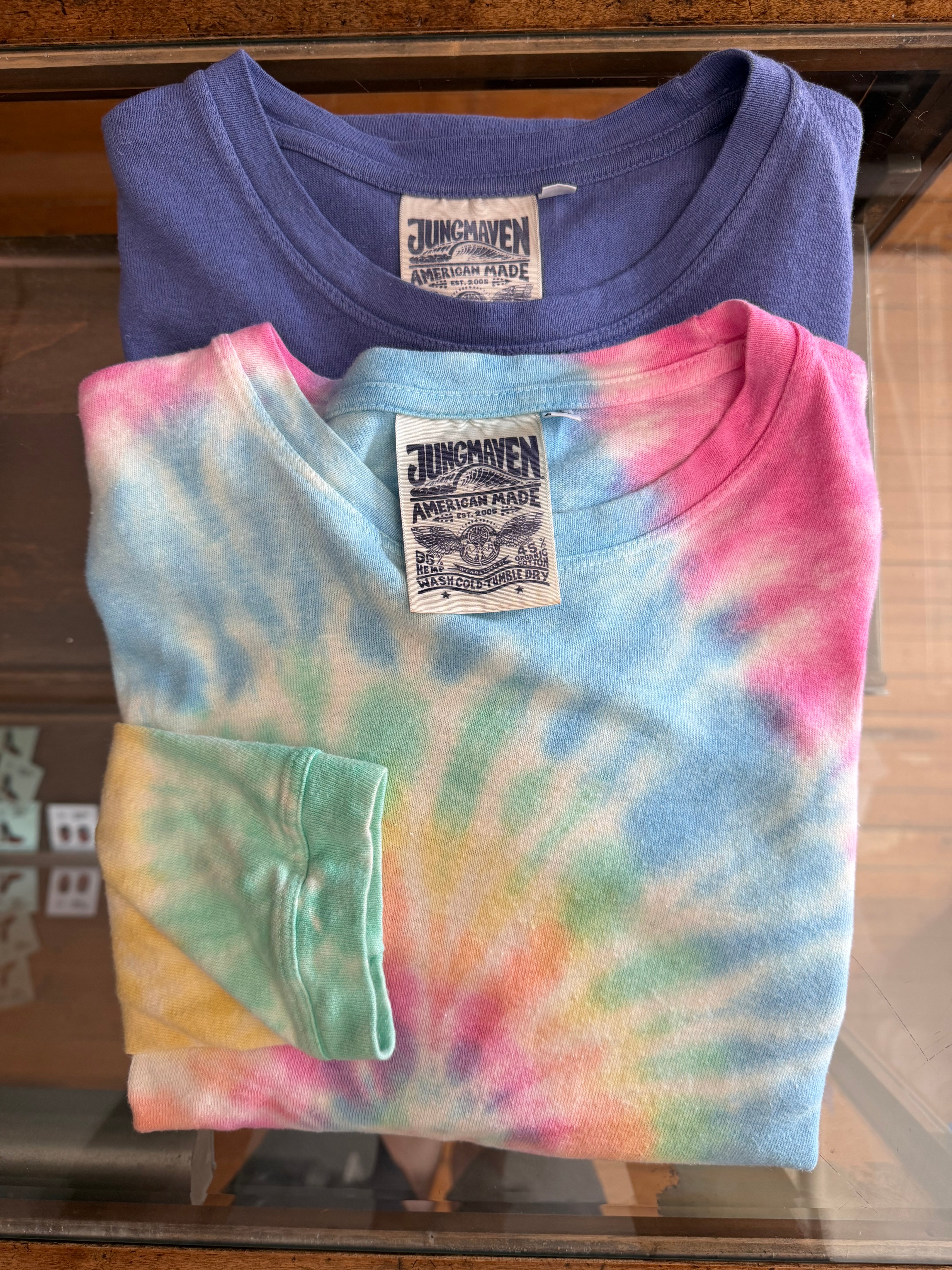 Front view of folded tie-dye and solid tees, showcasing Jungmaven tags and fabric texture.