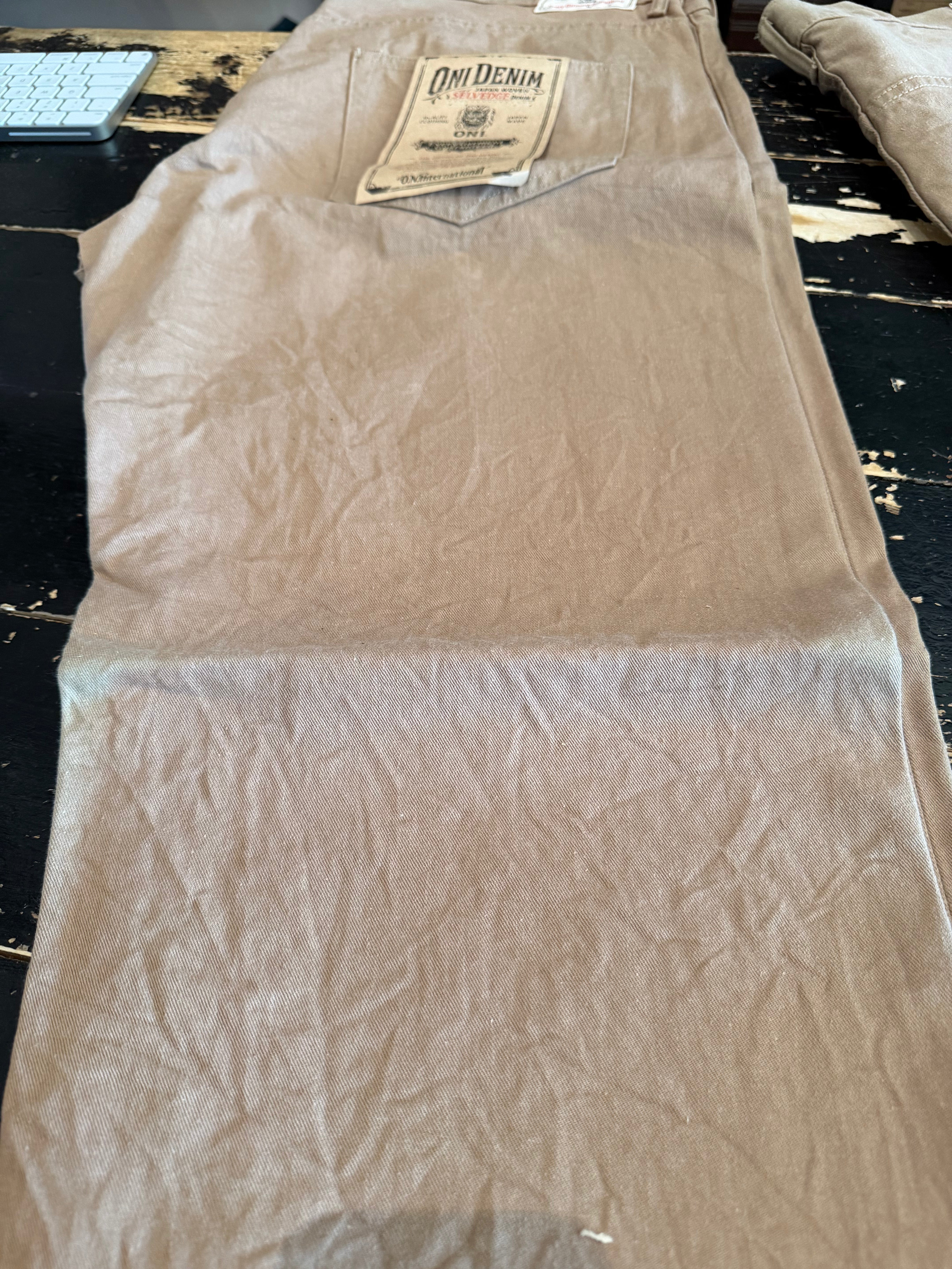 Flat lay, back view of tan selvedge denim jeans focusing on pocket and branded patch detail.