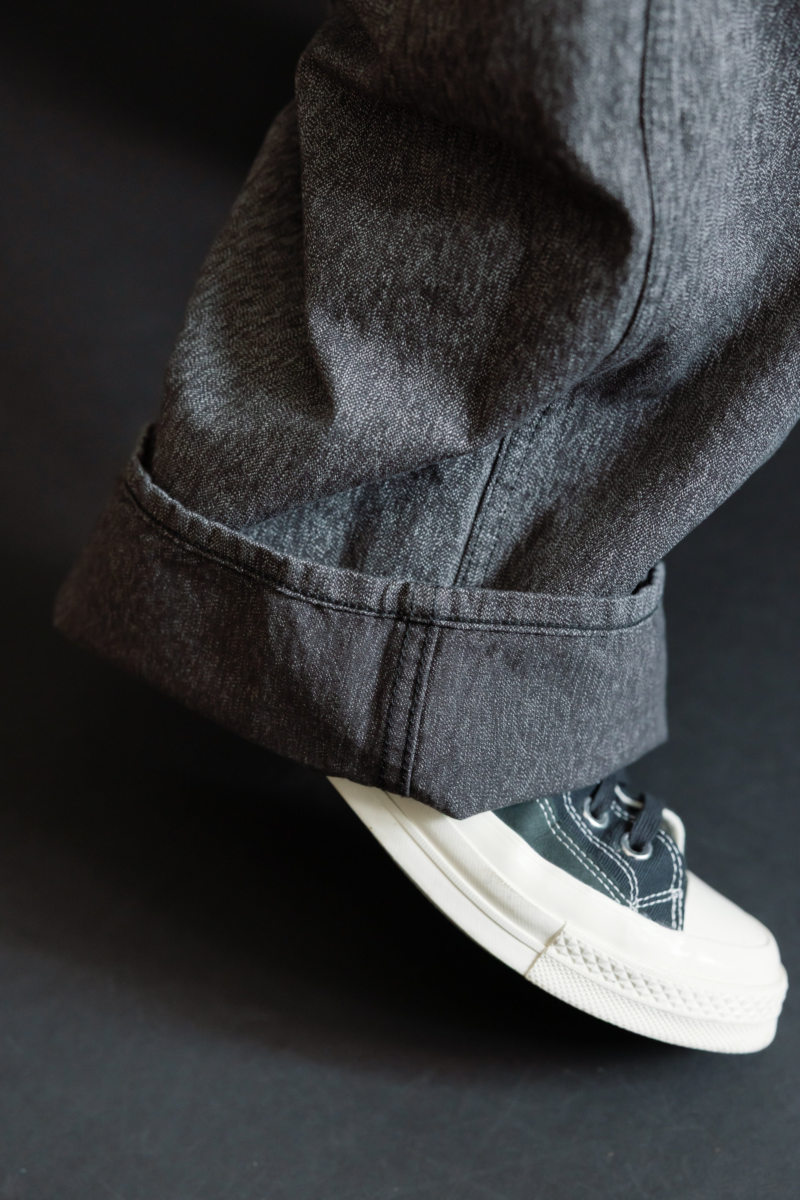 Close-up of dark selvedge denim pants hem, cuffed, worn by male model with athletic build, paired with white sneakers