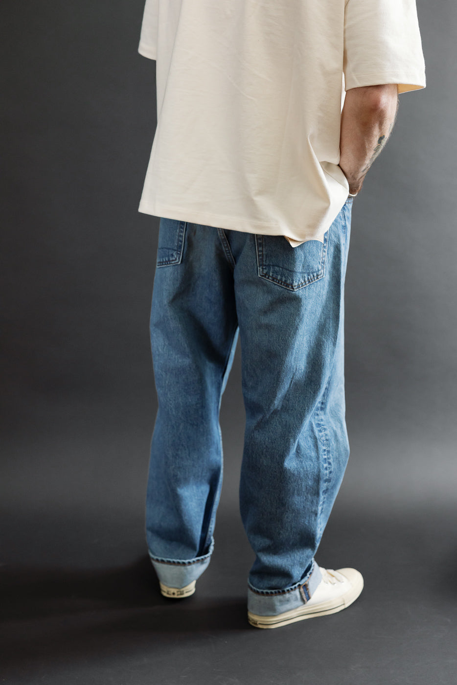 Back view, full body of a male model wearing baggy blue selvedge denim jeans and a white t-shirt.