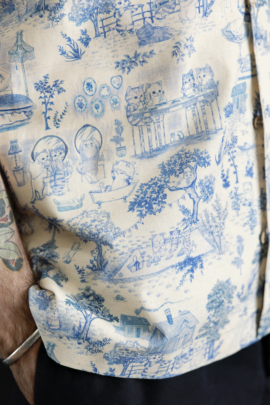 Close-up of front side of men's linen aloha shirt, blue cat print, button detail visible.