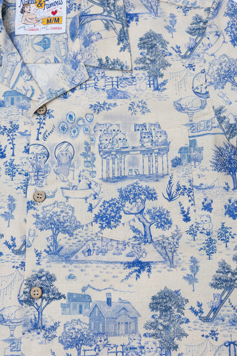 Close-up of front chest area of blue linen aloha shirt, showing cat print, collar, buttons, and pocket details.