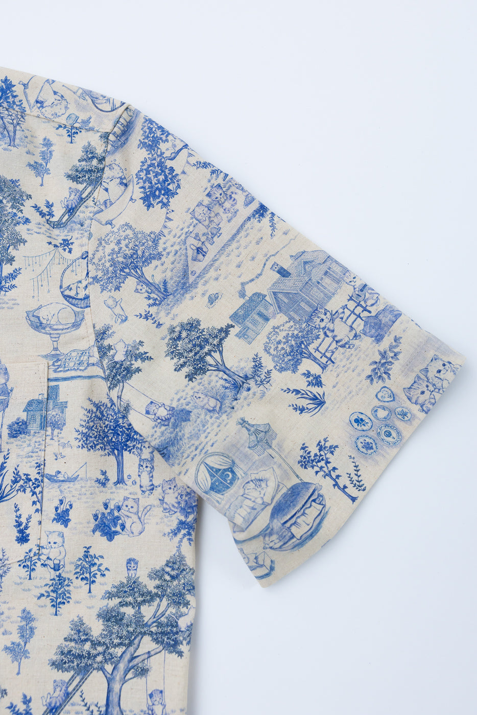 Close-up of aloha shirt linen sleeve, left side, with blue cat and village print fabric texture.
