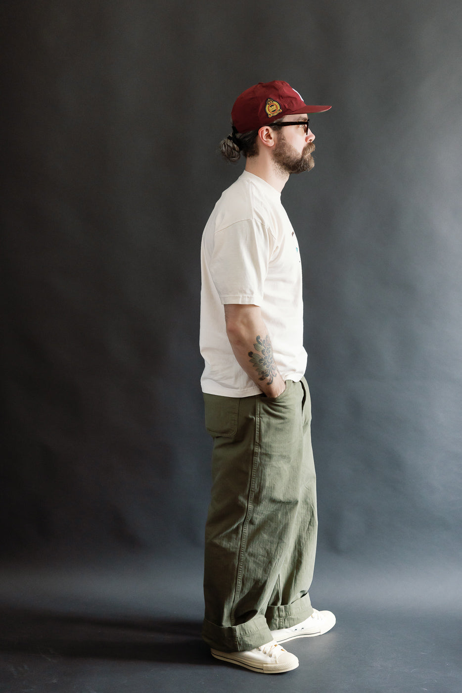 Man in profile wearing the 6.5oz Dant Blue-footed Booby T-Shirt in ecru, featuring a custom print and thick ribbed collar, paired with olive-green trousers and off-white sneakers.