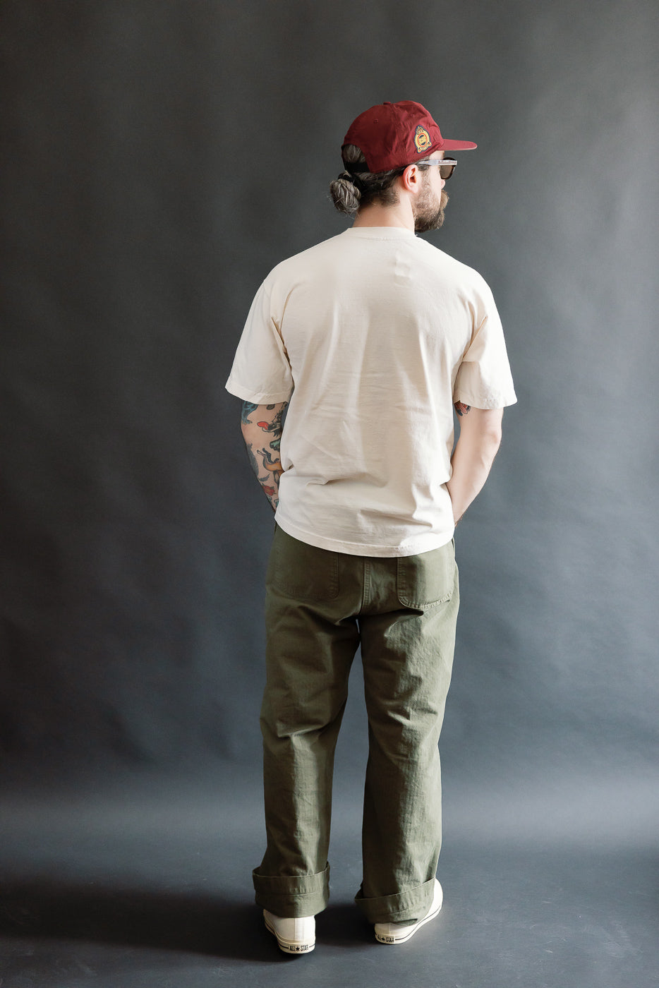 The 6.5oz Dant Blue Footed Booby T-Shirt in Ecru, worn by a 5'9 Caucasian male model with tattoos, features a relaxed fit, capturing a playful bird design emblematic of Dant's heritage-inspired fashion ethos.
