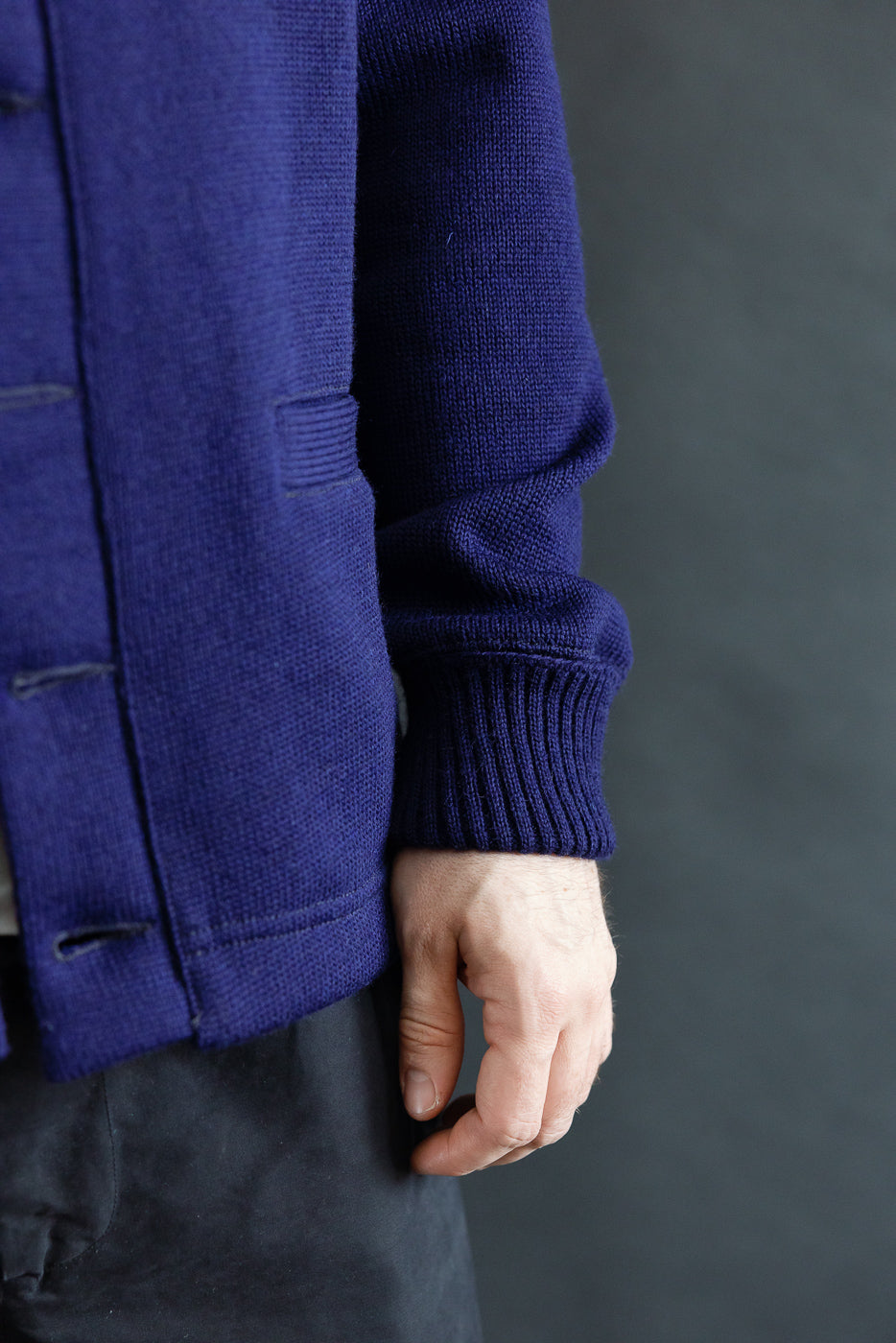 Close-up of male model's right side, showing ribbed sleeve cuff and waist of purple cardigan