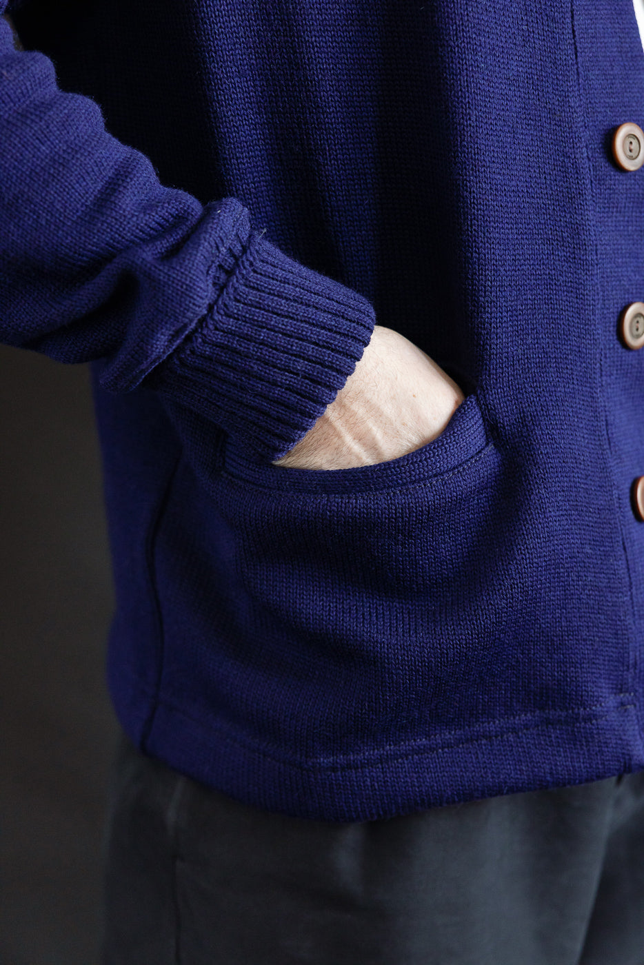 Close-up of male model's hand in front pocket, classic purple cardigan, ribbed cuff, button detail