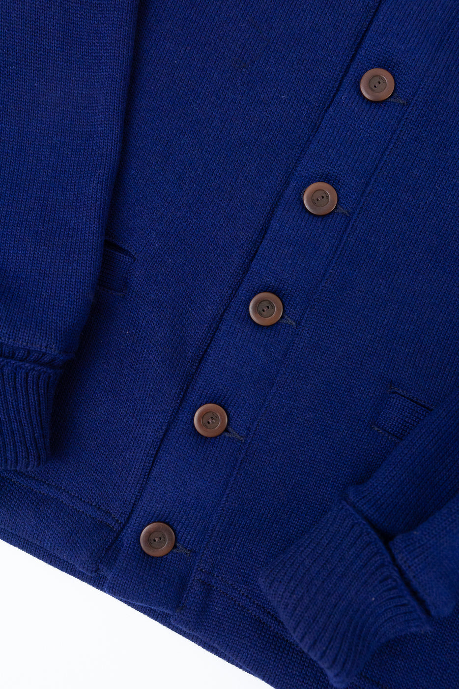 Close-up of front center of purple classic cardigan, showing brown buttons, knit cuffs, and texture.
