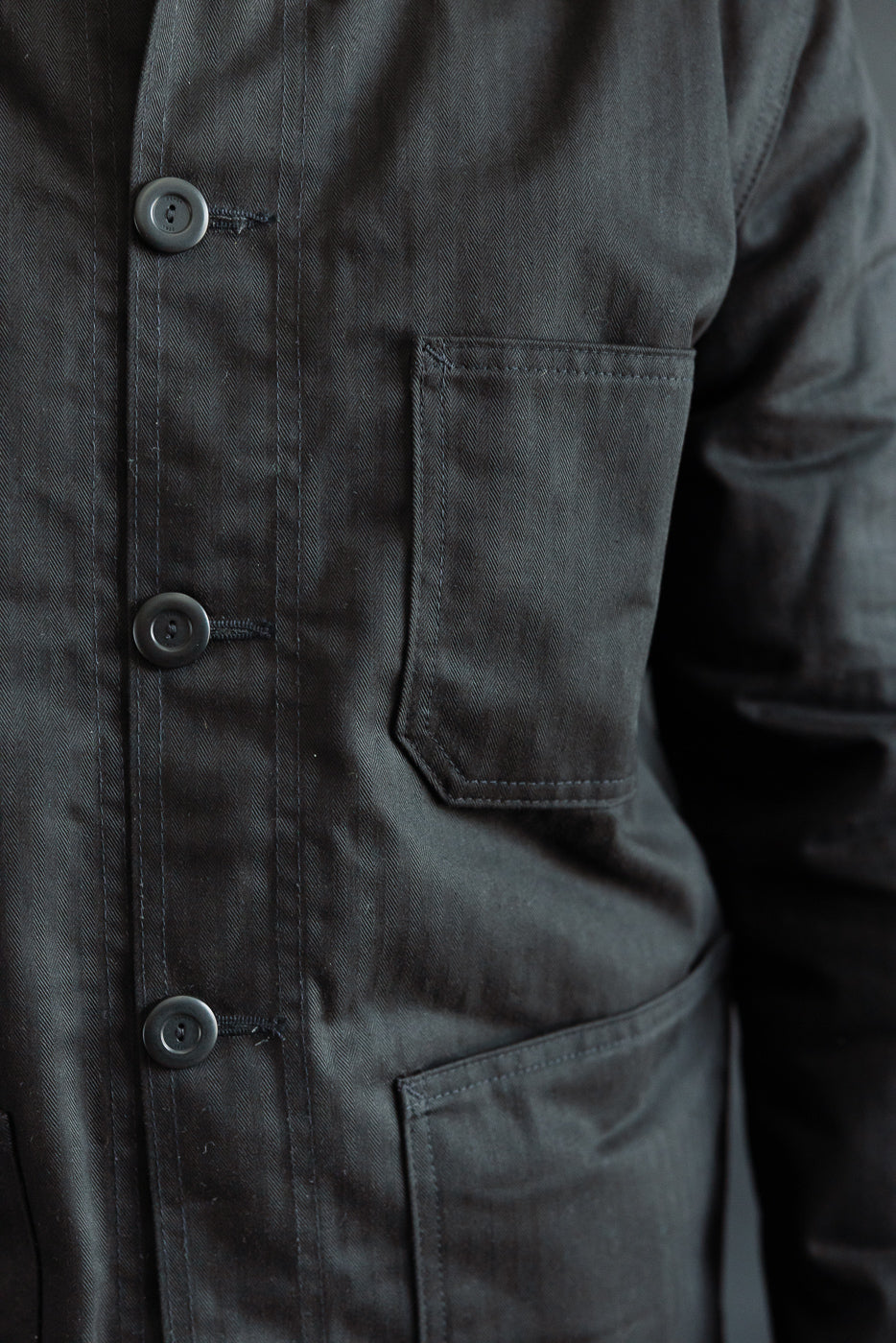 Close-up of front chest and waist pockets, black chore coat, button detail, left side.