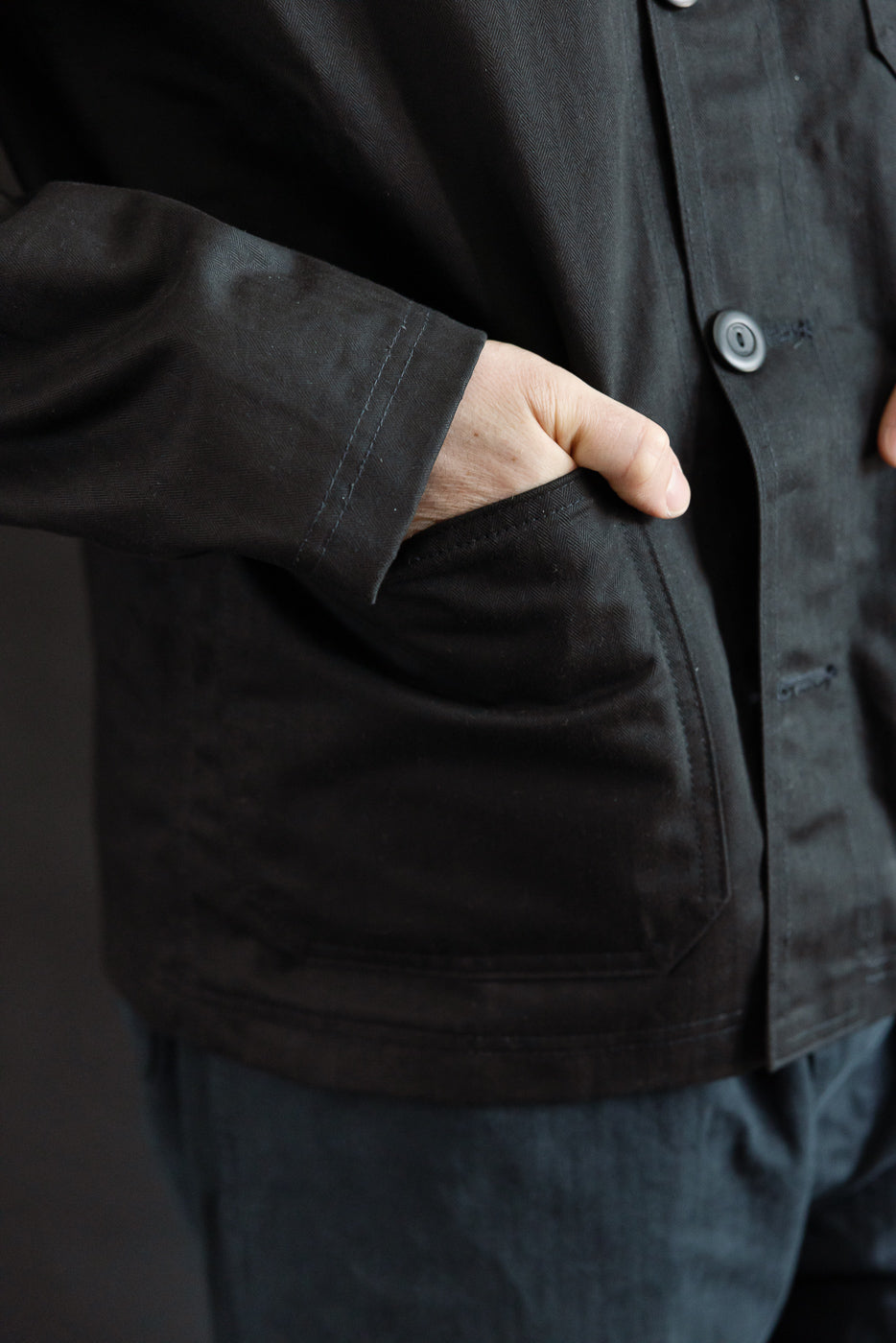 Close-up of front left side of black chore coat on male model, showing pocket detail and button.