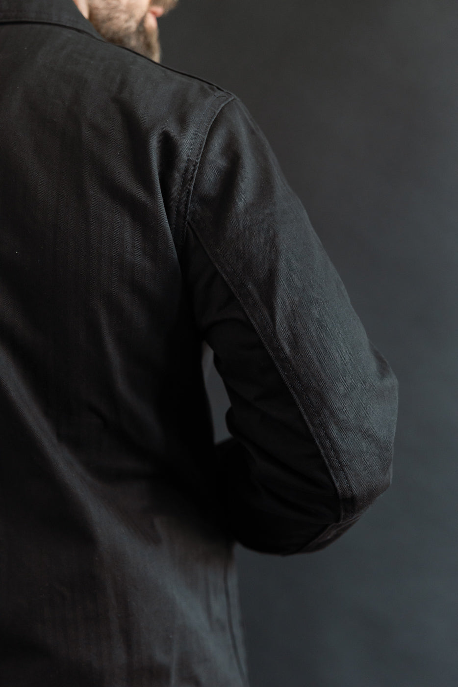 Close-up of back right shoulder and sleeve of black dry wax chore coat on male model, 5'9
