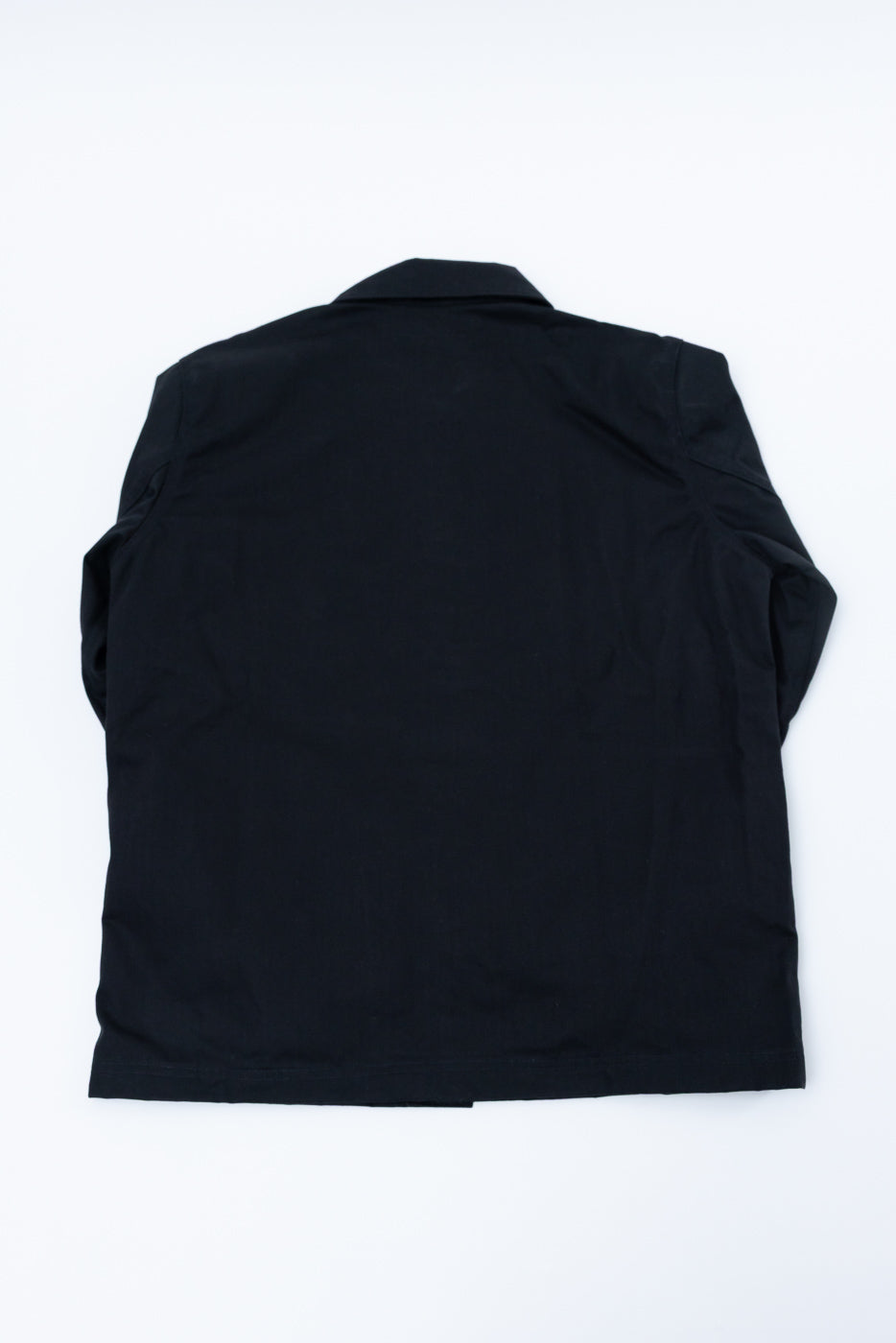 Flat lay of chore coat, back view, showing black dry wax woven fabric and straight hem.