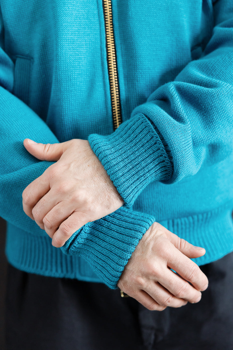 Close-up of male model's hands wearing aqua full-zip moto hoodie, showing front cuffs and zipper, 5'9